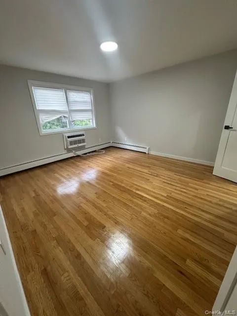 Spare room featuring light wood-type flooring, a wall unit AC, and baseboard heating Spare room featuring light wood-type flooring, a wall unit AC, and baseboard heating