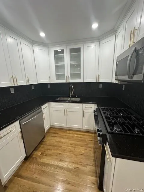 Kitchen featuring stainless steel appliances, white cabinetry, decorative backsplash, glass insert cabinets, and light wood-type flooring Kitchen featuring stainless steel appliances, white cabinetry, decorative backsplash, glass insert cabinets, and light wood-type flooring