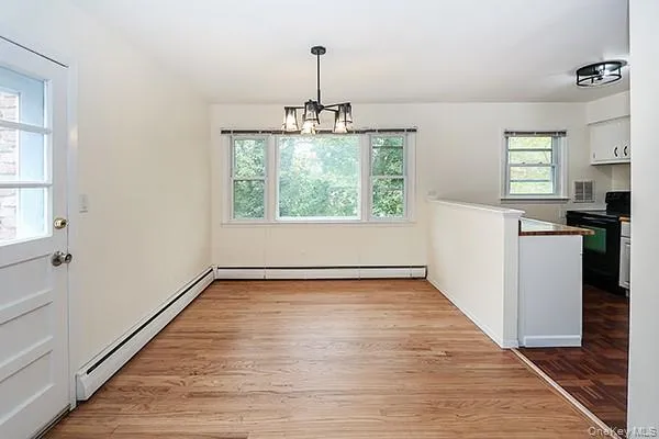 Unfurnished dining area featuring baseboard heating, light wood-style flooring, and a chandelier Unfurnished dining area featuring baseboard heating, light wood-style flooring, and a chandelier