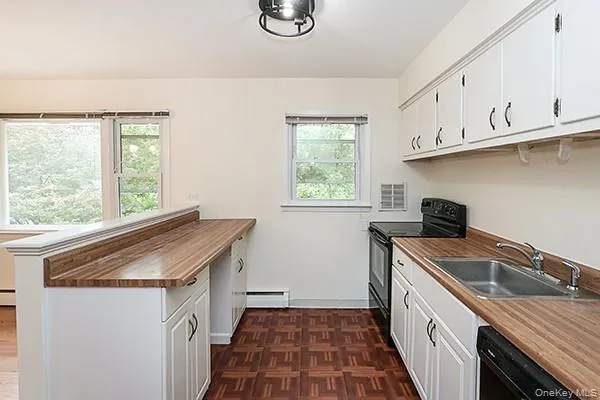 Kitchen with a peninsula, black appliances, white cabinets, a baseboard radiator, and wooden counters Kitchen with a peninsula, black appliances, white cabinets, a baseboard radiator, and wooden counters