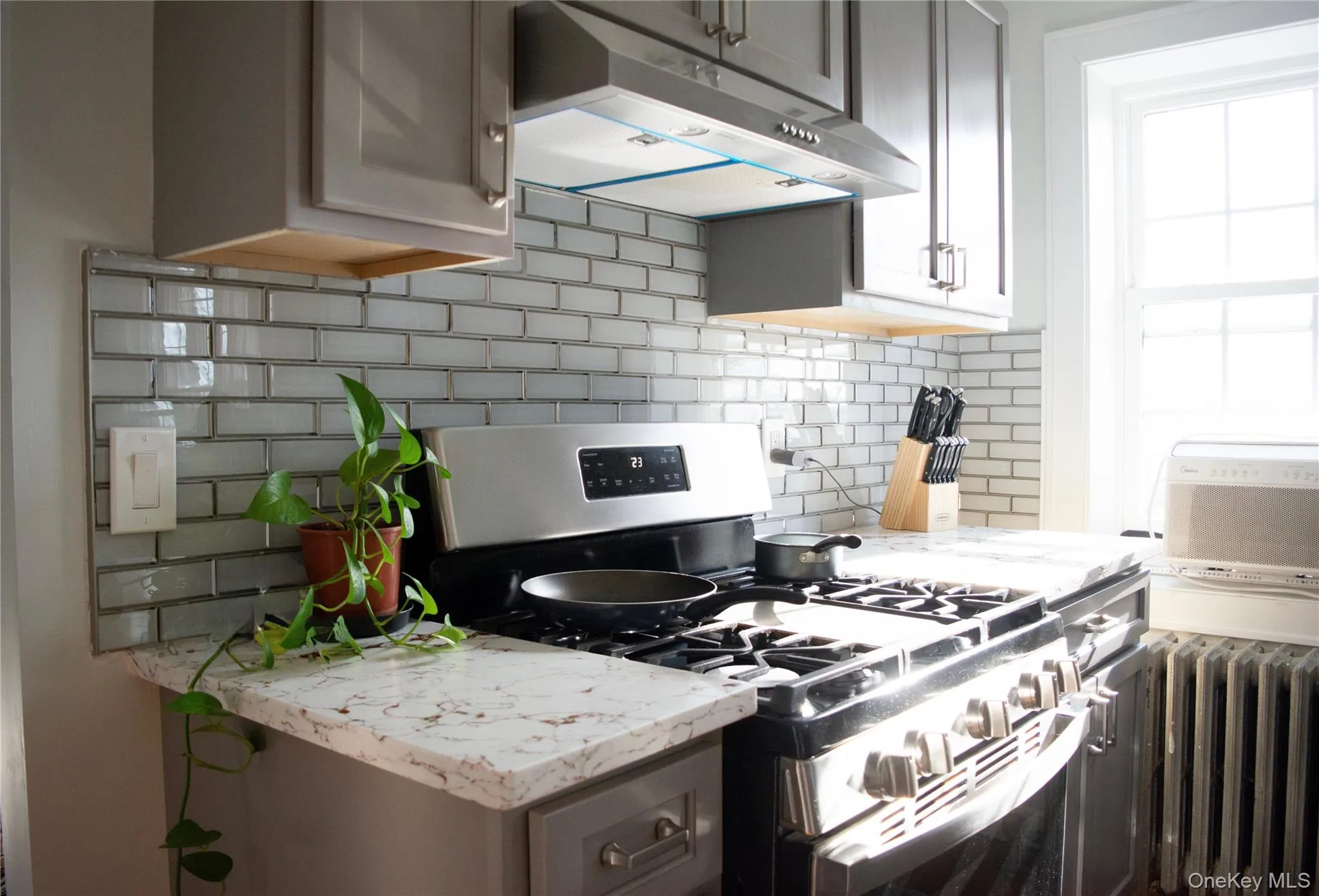 Kitchen with stainless steel gas range, backsplash, under cabinet range hood, radiator heating unit, and light stone countertops Kitchen with stainless steel gas range, backsplash, under cabinet range hood, radiator heating unit, and light stone countertops