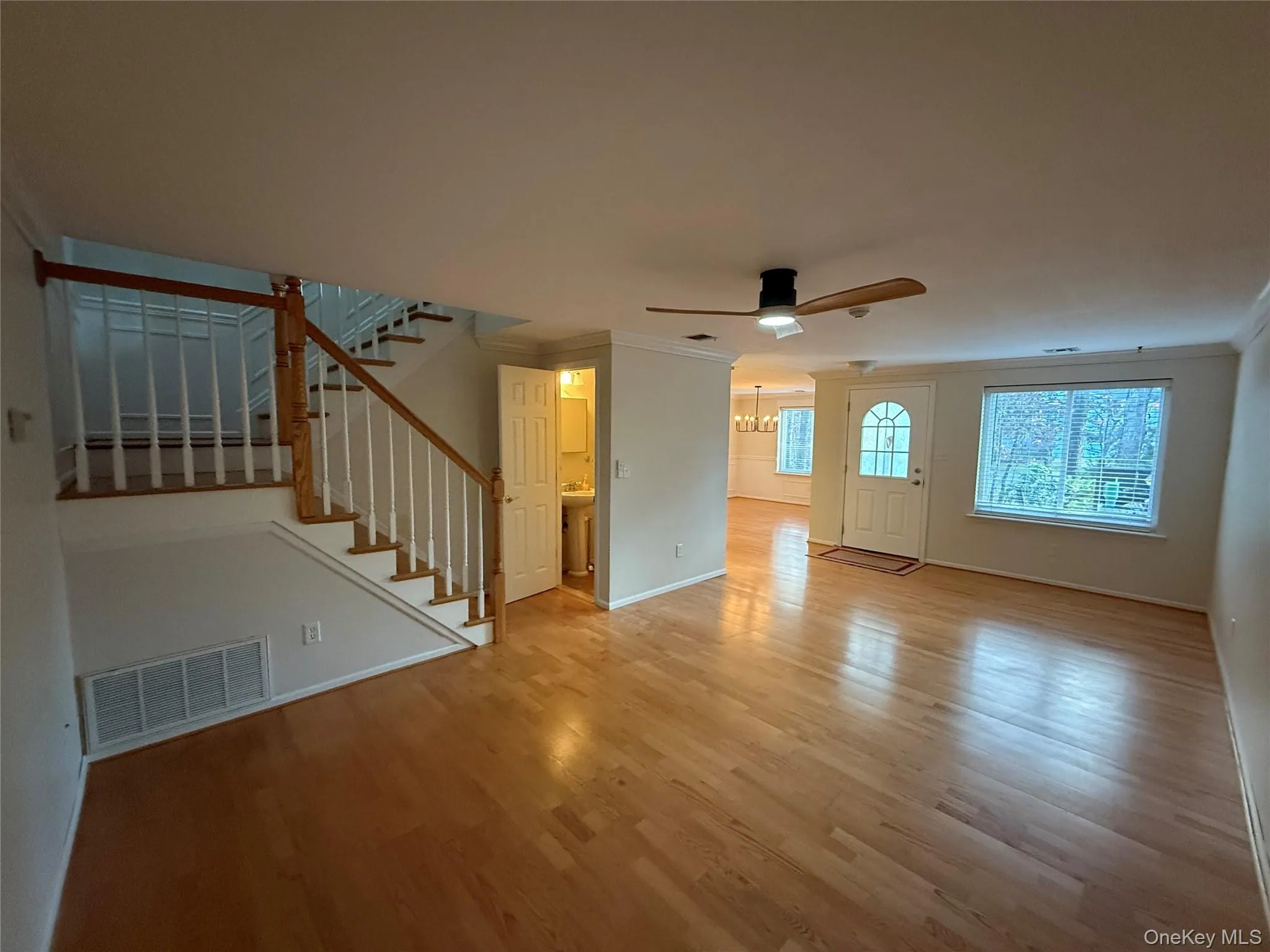 Unfurnished living room with ornamental molding, light wood-style flooring, stairway, ceiling fan, and a chandelier Unfurnished living room with ornamental molding, light wood-style flooring, stairway, ceiling fan, and a chandelier