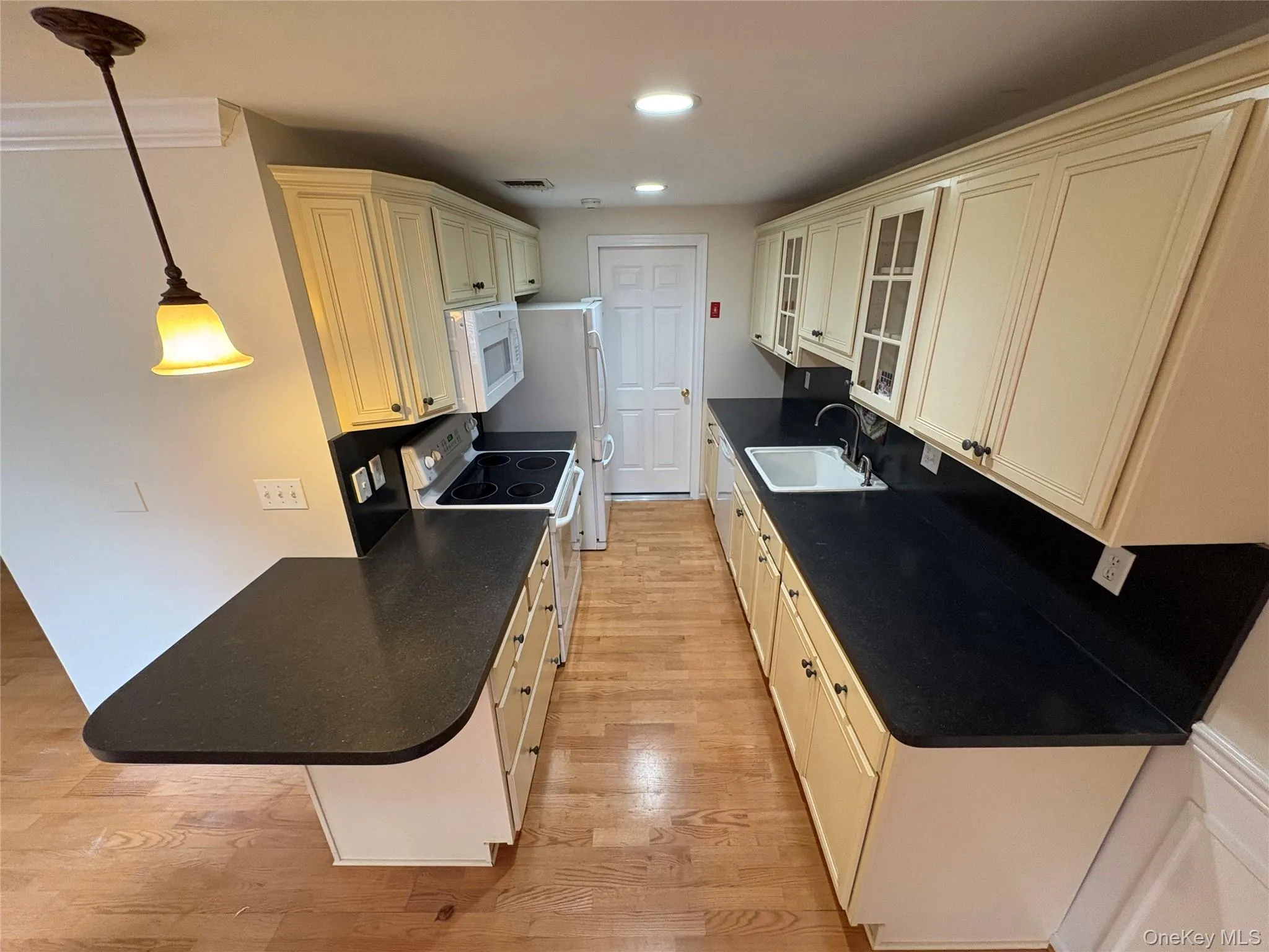 Kitchen with glass insert cabinets, white appliances, light wood-style flooring, recessed lighting, and a peninsula Kitchen with glass insert cabinets, white appliances, light wood-style flooring, recessed lighting, and a peninsula