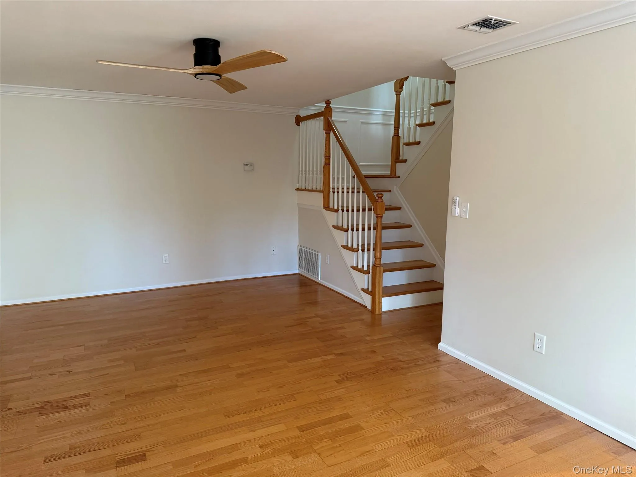 Unfurnished living room with ornamental molding, stairway, light wood finished floors, and a ceiling fan Unfurnished living room with ornamental molding, stairway, light wood finished floors, and a ceiling fan