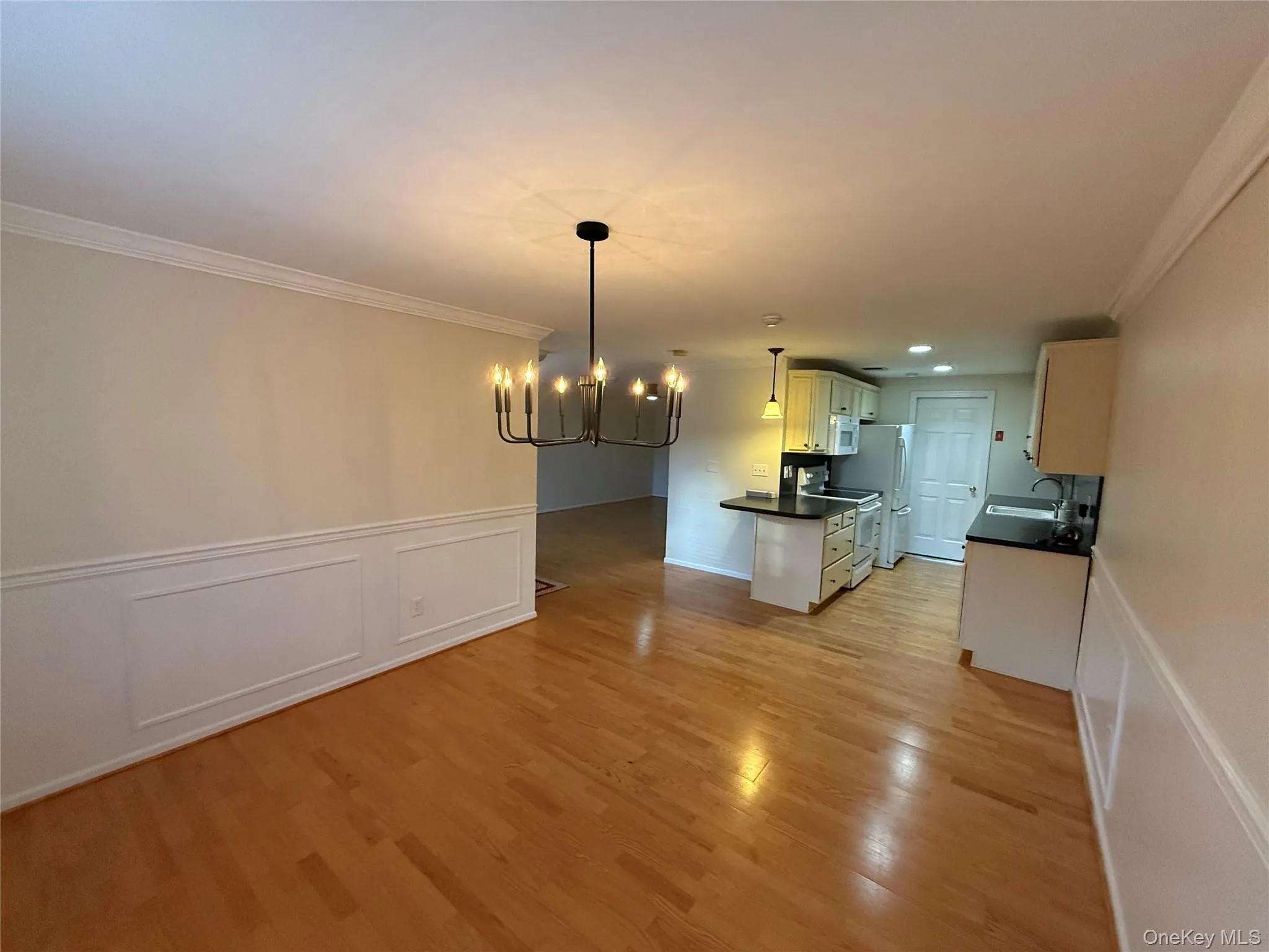 Kitchen with dark countertops, ornamental molding, a wainscoted wall, a decorative wall, and a chandelier Kitchen with dark countertops, ornamental molding, a wainscoted wall, a decorative wall, and a chandelier