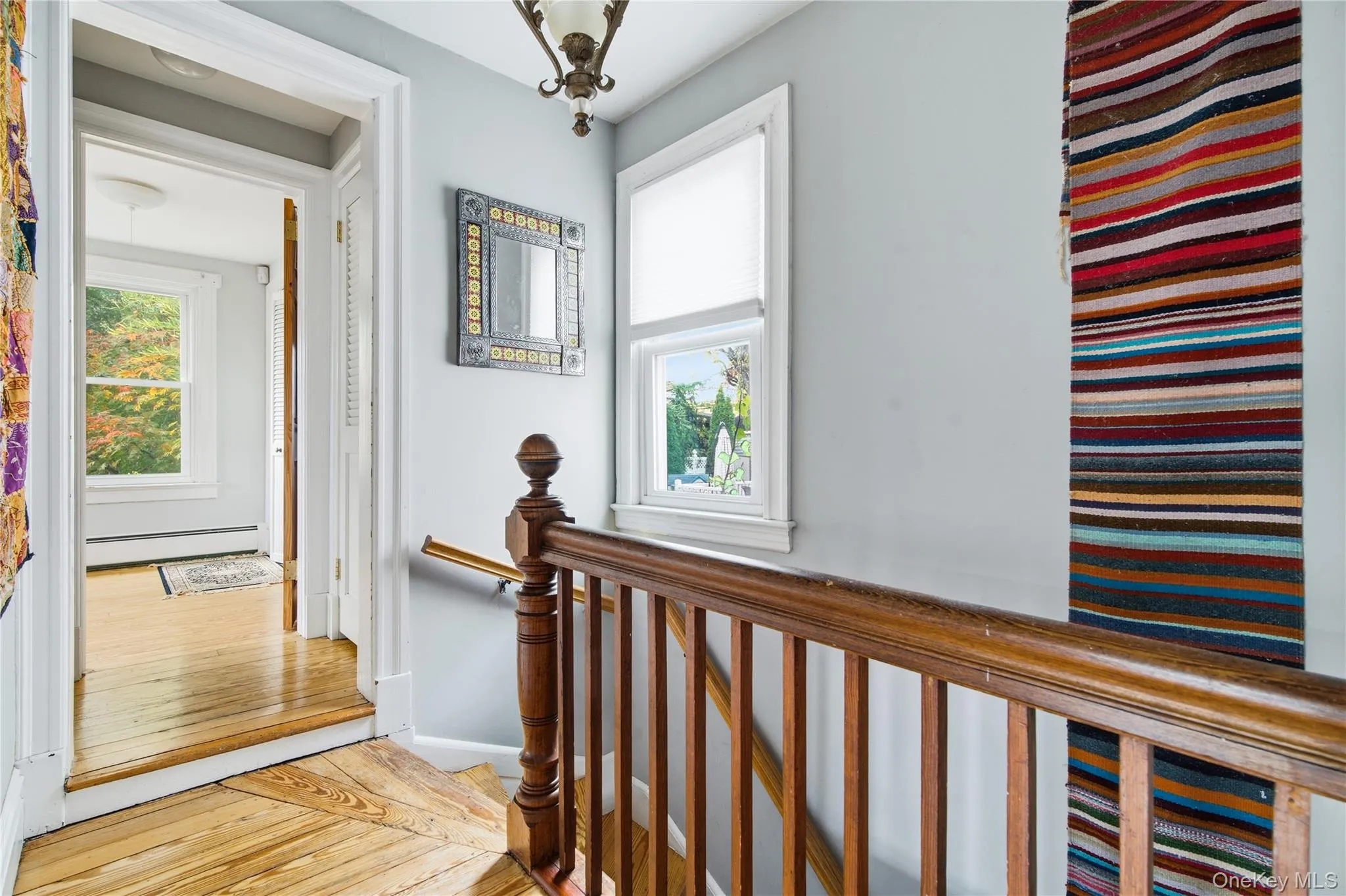 Hall featuring a baseboard heating unit, light wood-style floors, an upstairs landing, and healthy amount of natural light Hall featuring a baseboard heating unit, light wood-style floors, an upstairs landing, and healthy amount of natural light