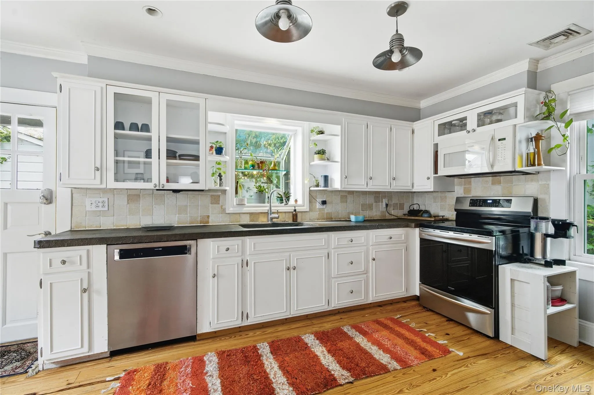 Kitchen featuring open shelves, glass insert cabinets, stainless steel appliances, white cabinetry, and plenty of natural light Kitchen featuring open shelves, glass insert cabinets, stainless steel appliances, white cabinetry, and plenty of natural light