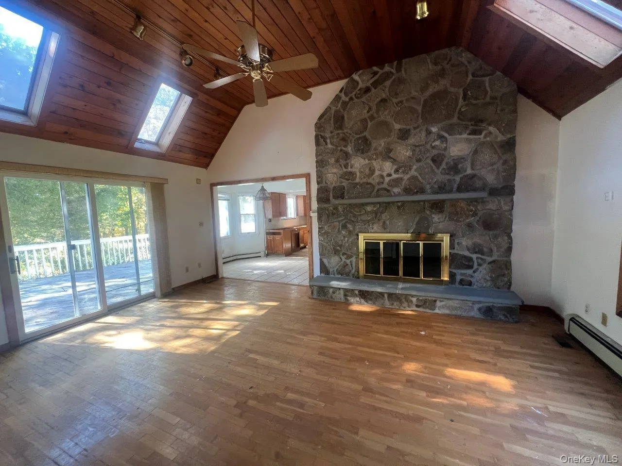 Unfurnished living room featuring high vaulted ceiling, a skylight, wooden ceiling, wood finished floors, and a stone fireplace Unfurnished living room featuring high vaulted ceiling, a skylight, wooden ceiling, wood finished floors, and a stone fireplace