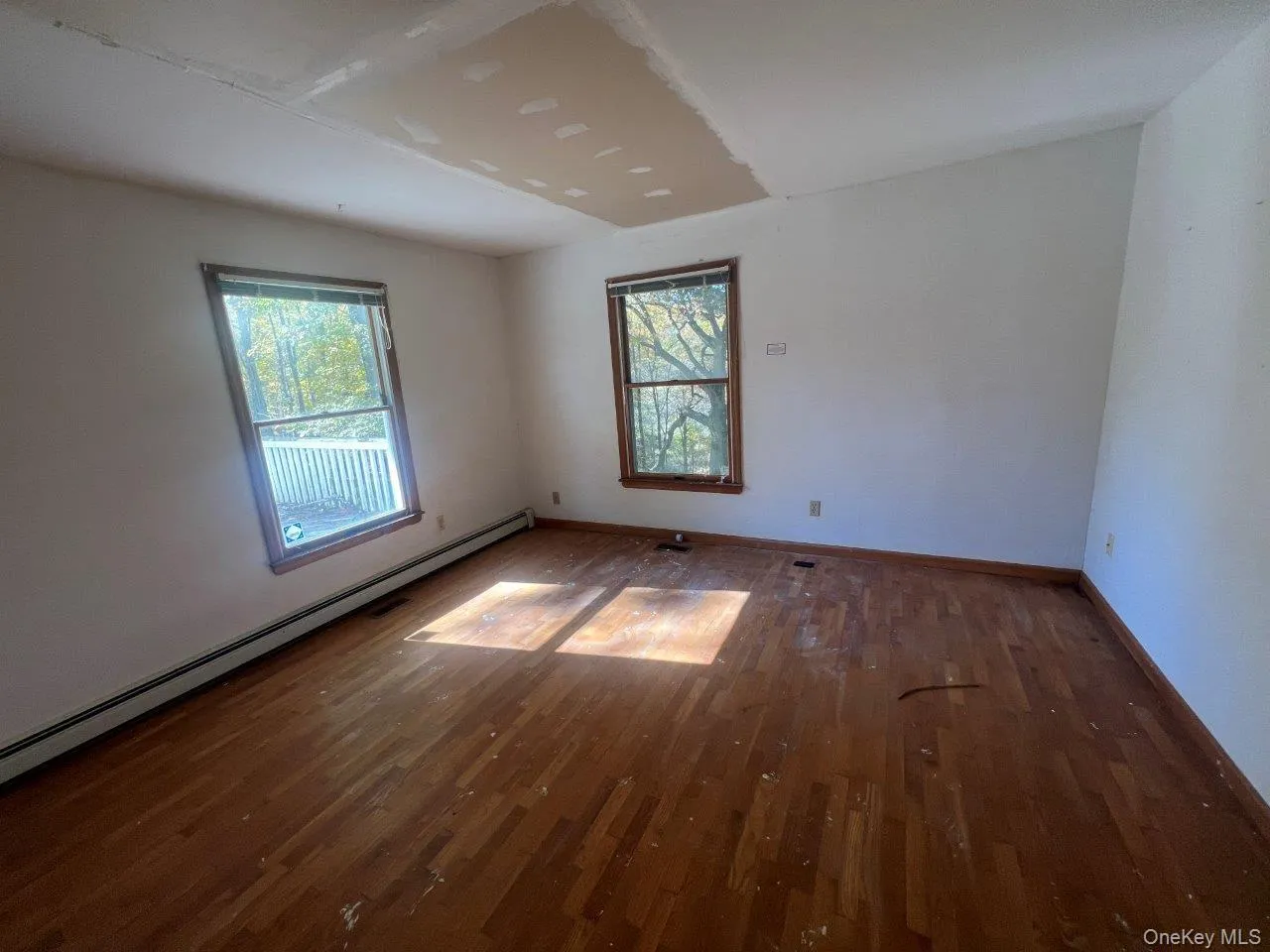Spare room with baseboard heating, wood finished floors, and plenty of natural light Spare room with baseboard heating, wood finished floors, and plenty of natural light