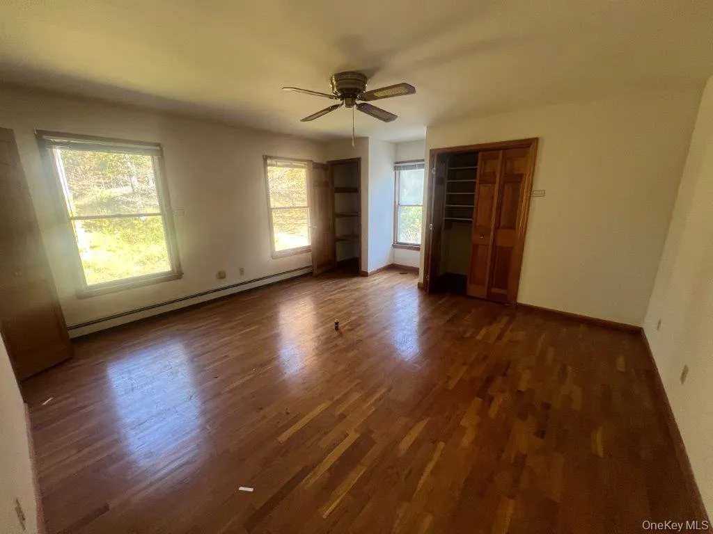 Unfurnished bedroom featuring a baseboard radiator, dark wood finished floors, ceiling fan, and two closets Unfurnished bedroom featuring a baseboard radiator, dark wood finished floors, ceiling fan, and two closets