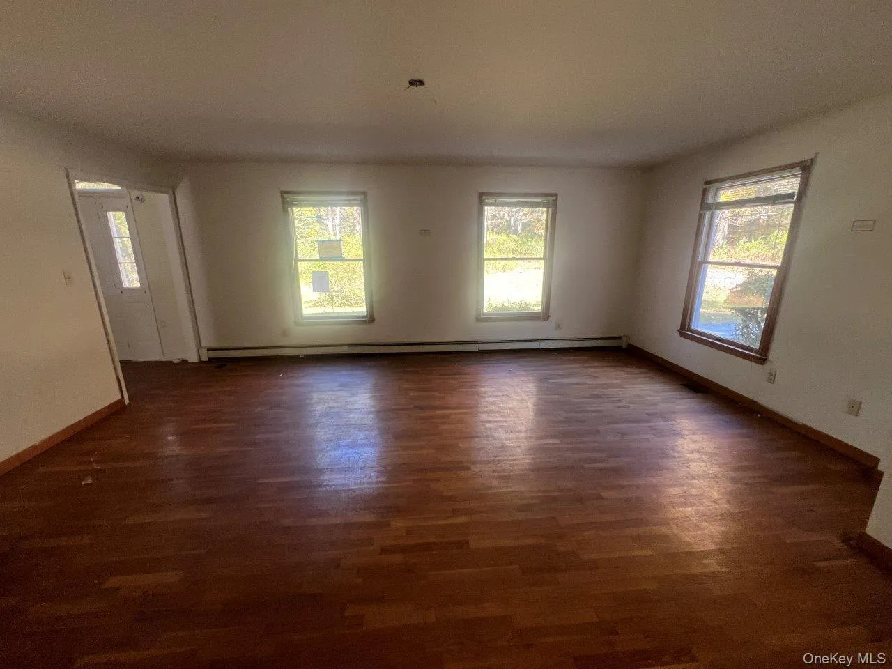 Unfurnished room with dark wood-type flooring and a baseboard heating unit Unfurnished room with dark wood-type flooring and a baseboard heating unit