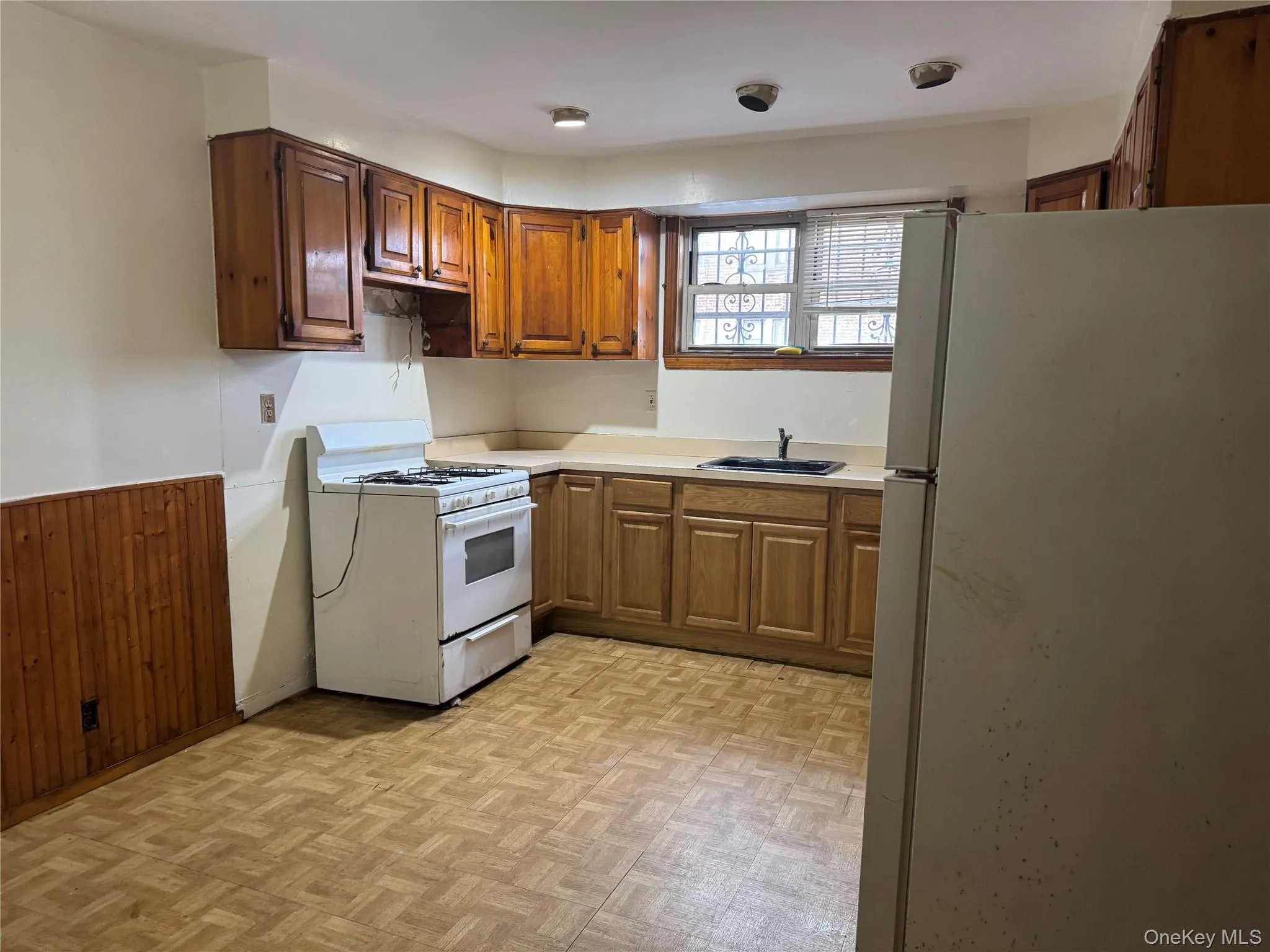 Kitchen featuring white appliances, wood walls, light countertops, brown cabinets, and a wainscoted wall Kitchen featuring white appliances, wood walls, light countertops, brown cabinets, and a wainscoted wall