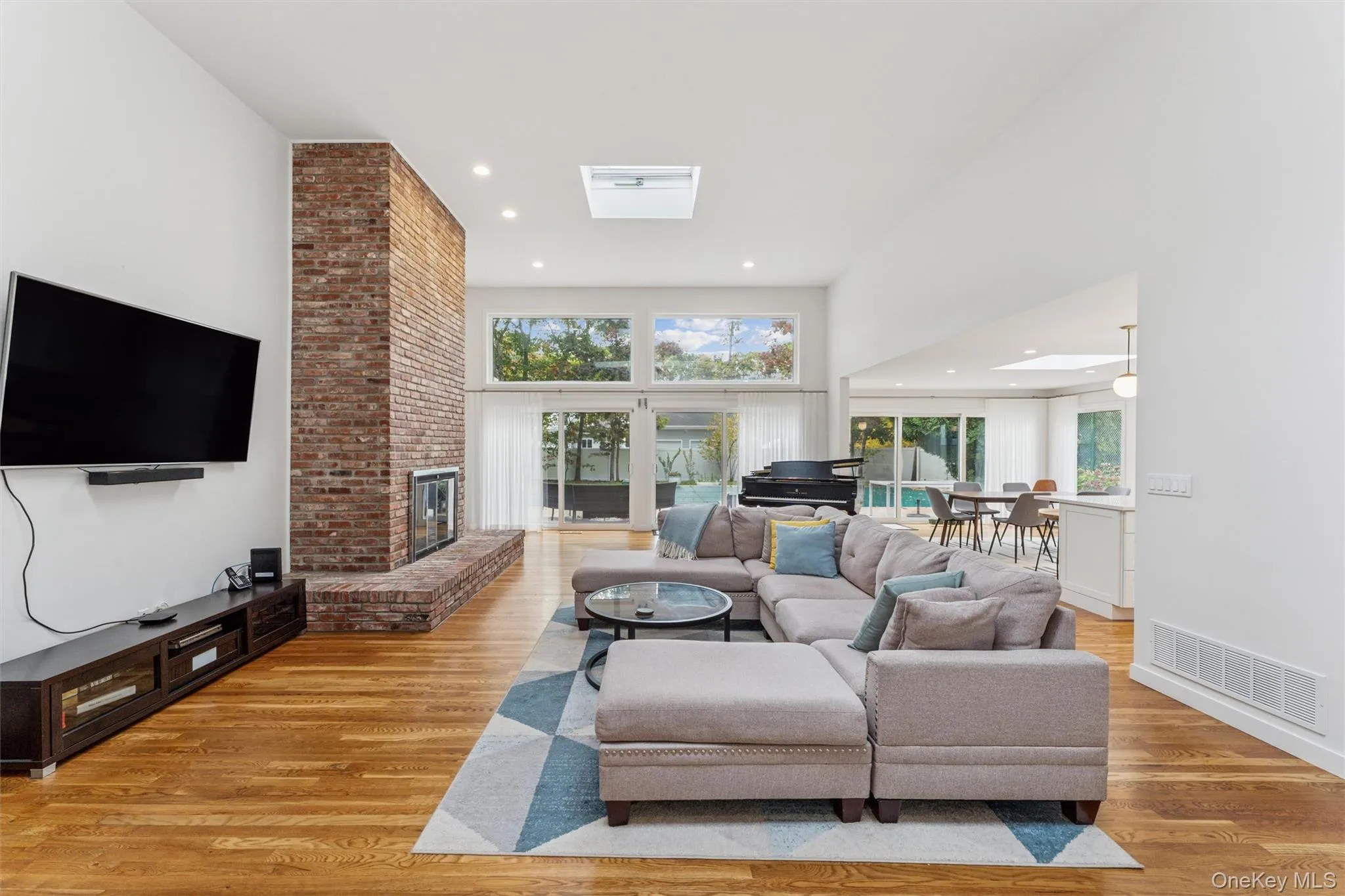 Living room with healthy amount of natural light, light wood-style flooring, recessed lighting, a high ceiling, and a brick fireplace Living room with healthy amount of natural light, light wood-style flooring, recessed lighting, a high ceiling, and a brick fireplace