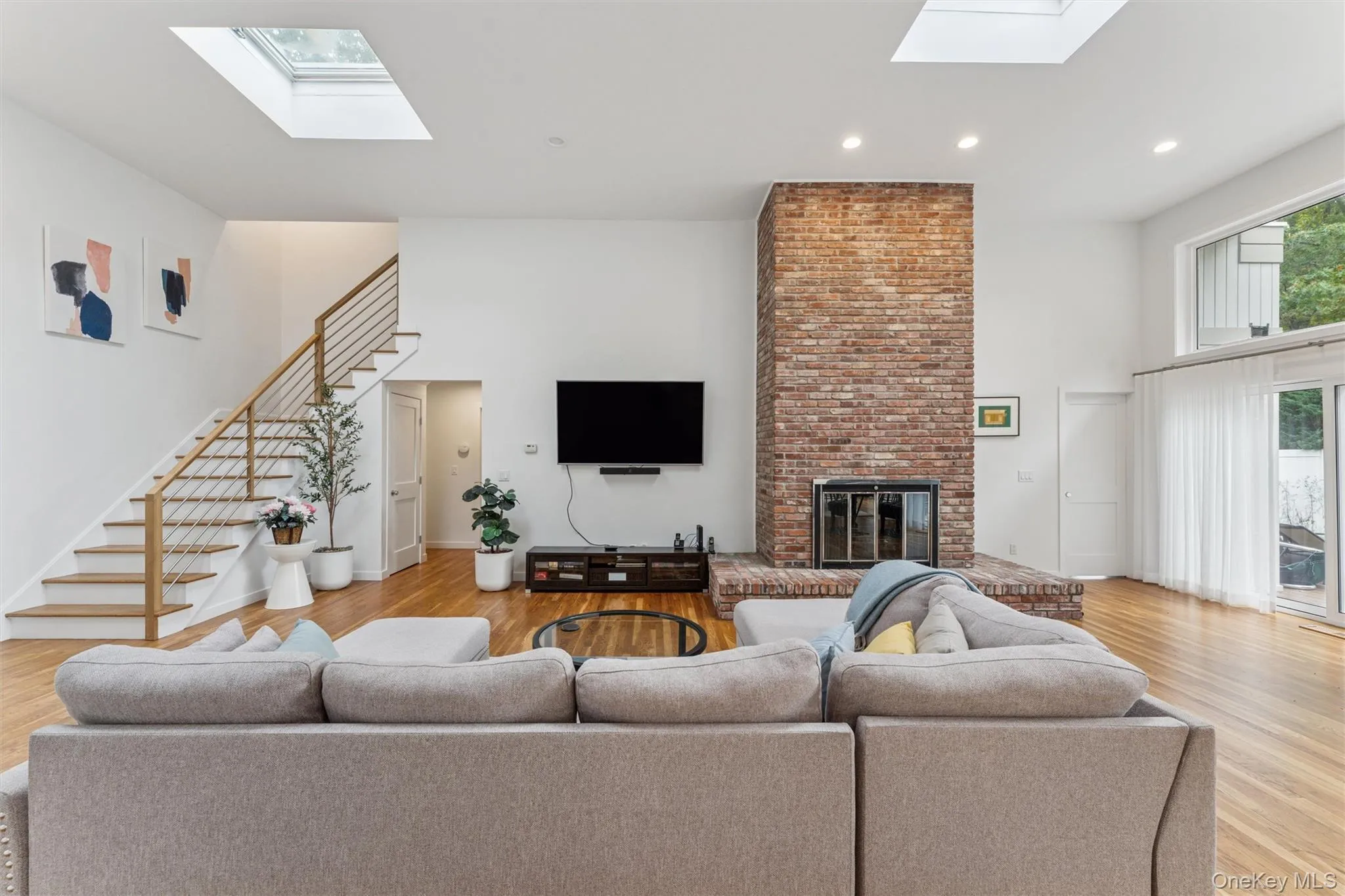 Living area featuring a skylight, light wood-style flooring, a fireplace, stairway, and a towering ceiling Living area featuring a skylight, light wood-style flooring, a fireplace, stairway, and a towering ceiling