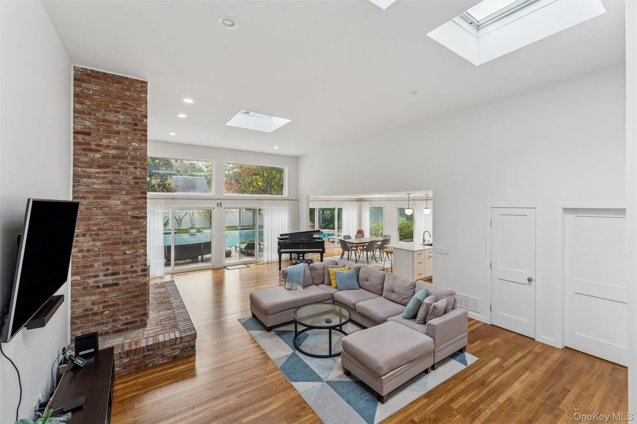 Living area featuring wood finished floors, a towering ceiling, recessed lighting, and a skylight Living area featuring wood finished floors, a towering ceiling, recessed lighting, and a skylight