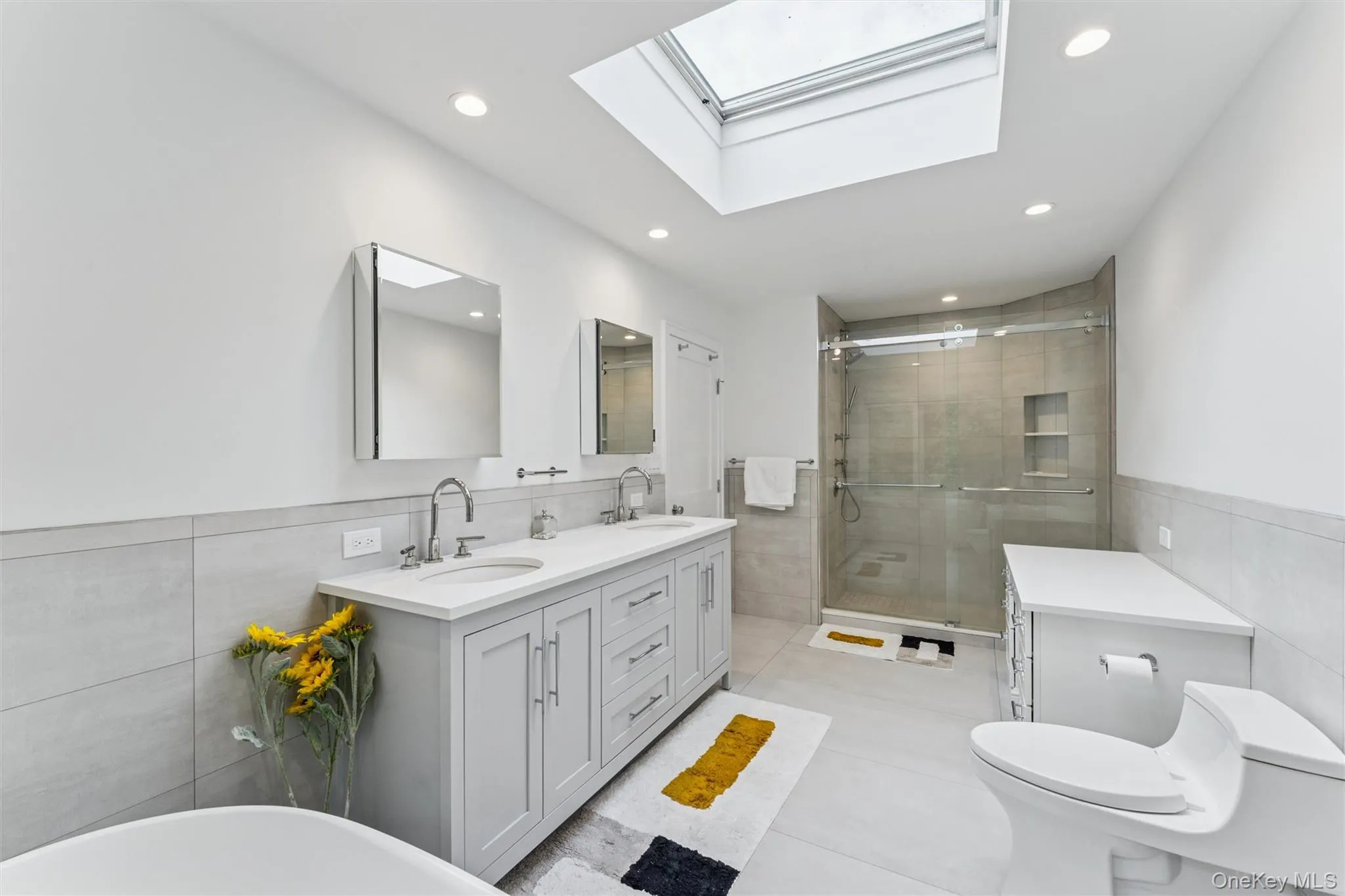 Bathroom featuring tile walls, wainscoting, double vanity, a skylight, and a stall shower Bathroom featuring tile walls, wainscoting, double vanity, a skylight, and a stall shower