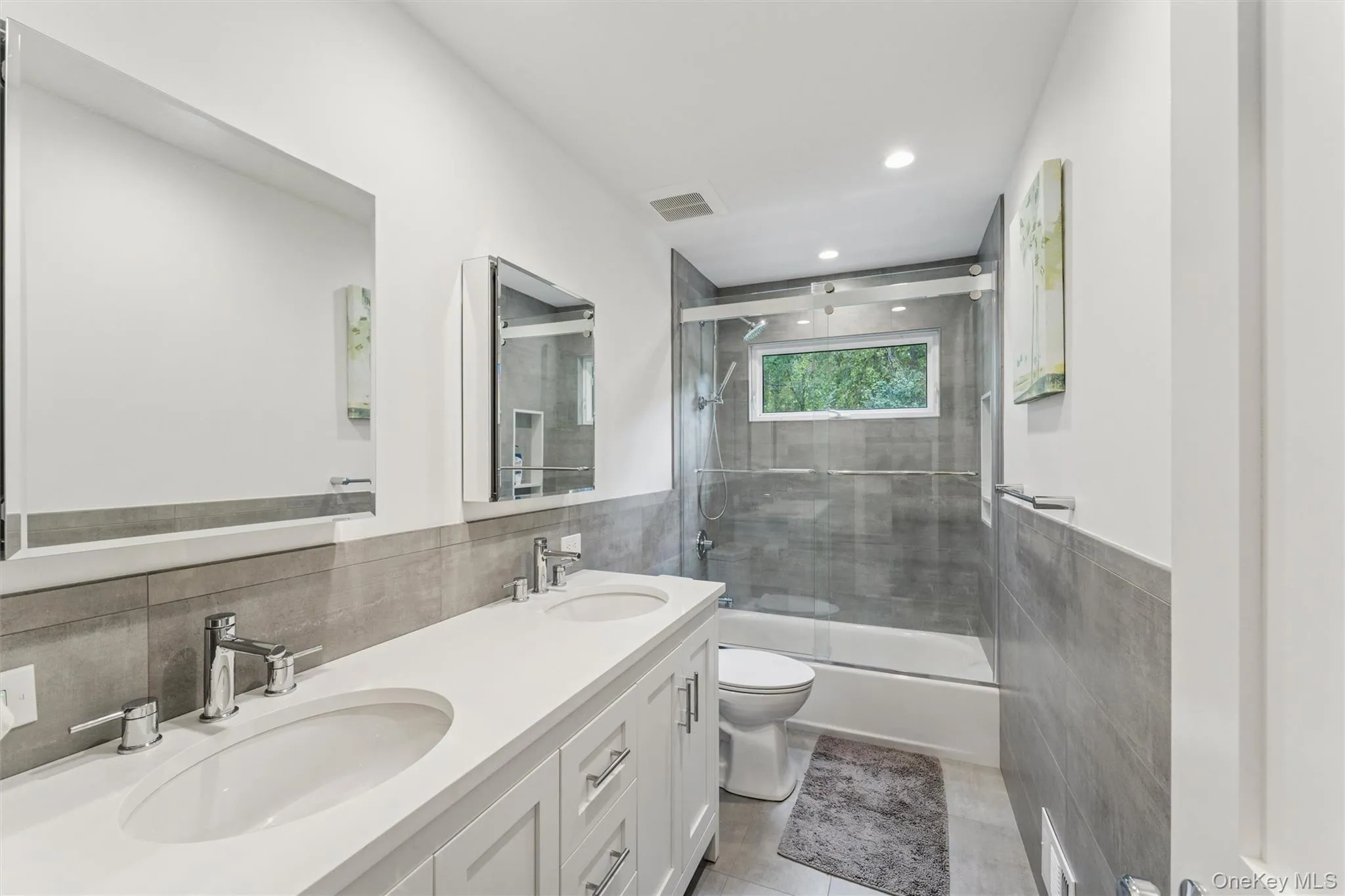 Full bathroom featuring tile walls, enclosed tub / shower combo, wainscoting, double vanity, and recessed lighting Full bathroom featuring tile walls, enclosed tub / shower combo, wainscoting, double vanity, and recessed lighting