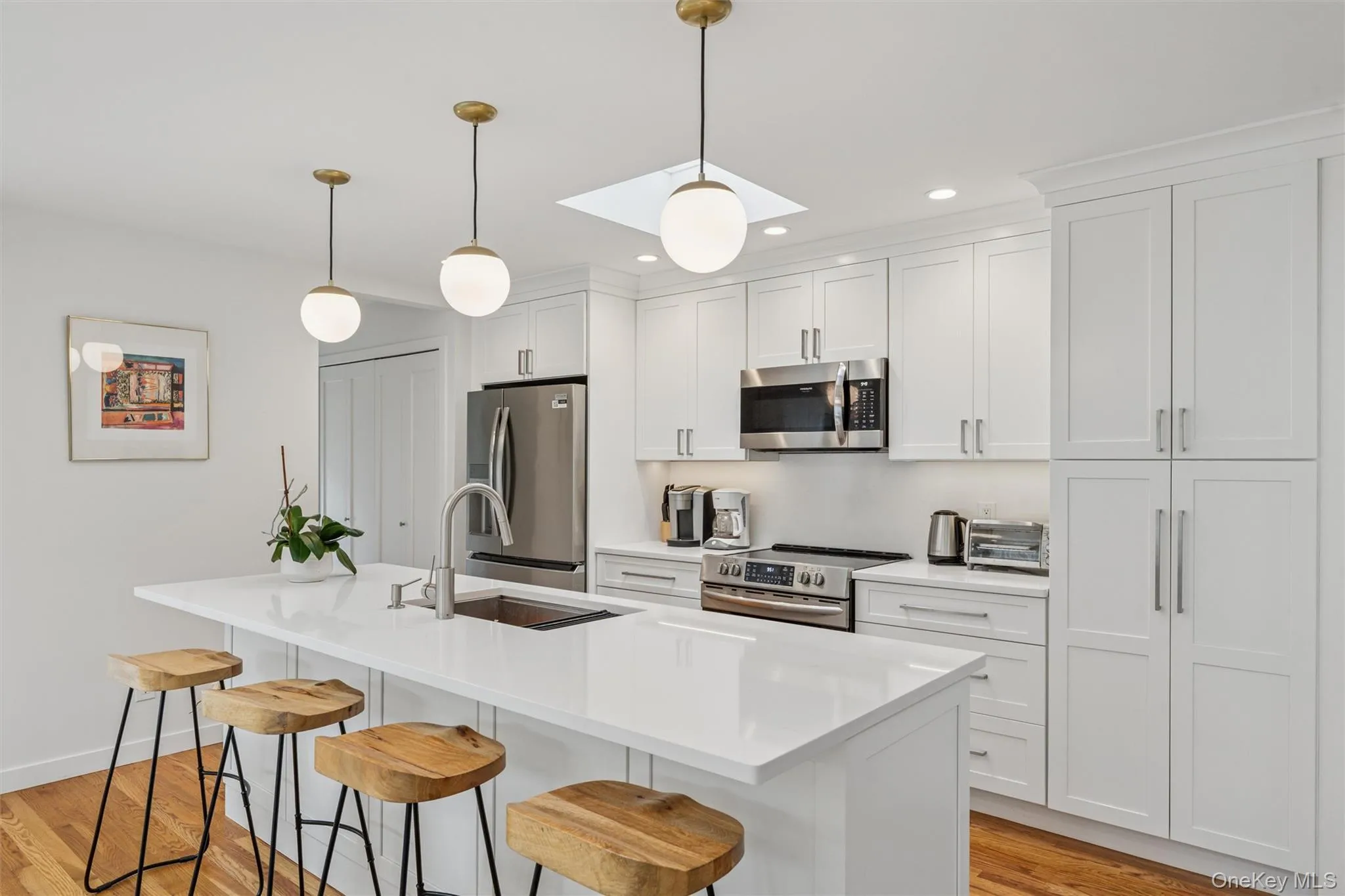 Kitchen with light wood-style floors, stainless steel appliances, pendant lighting, white cabinets, and recessed lighting Kitchen with light wood-style floors, stainless steel appliances, pendant lighting, white cabinets, and recessed lighting