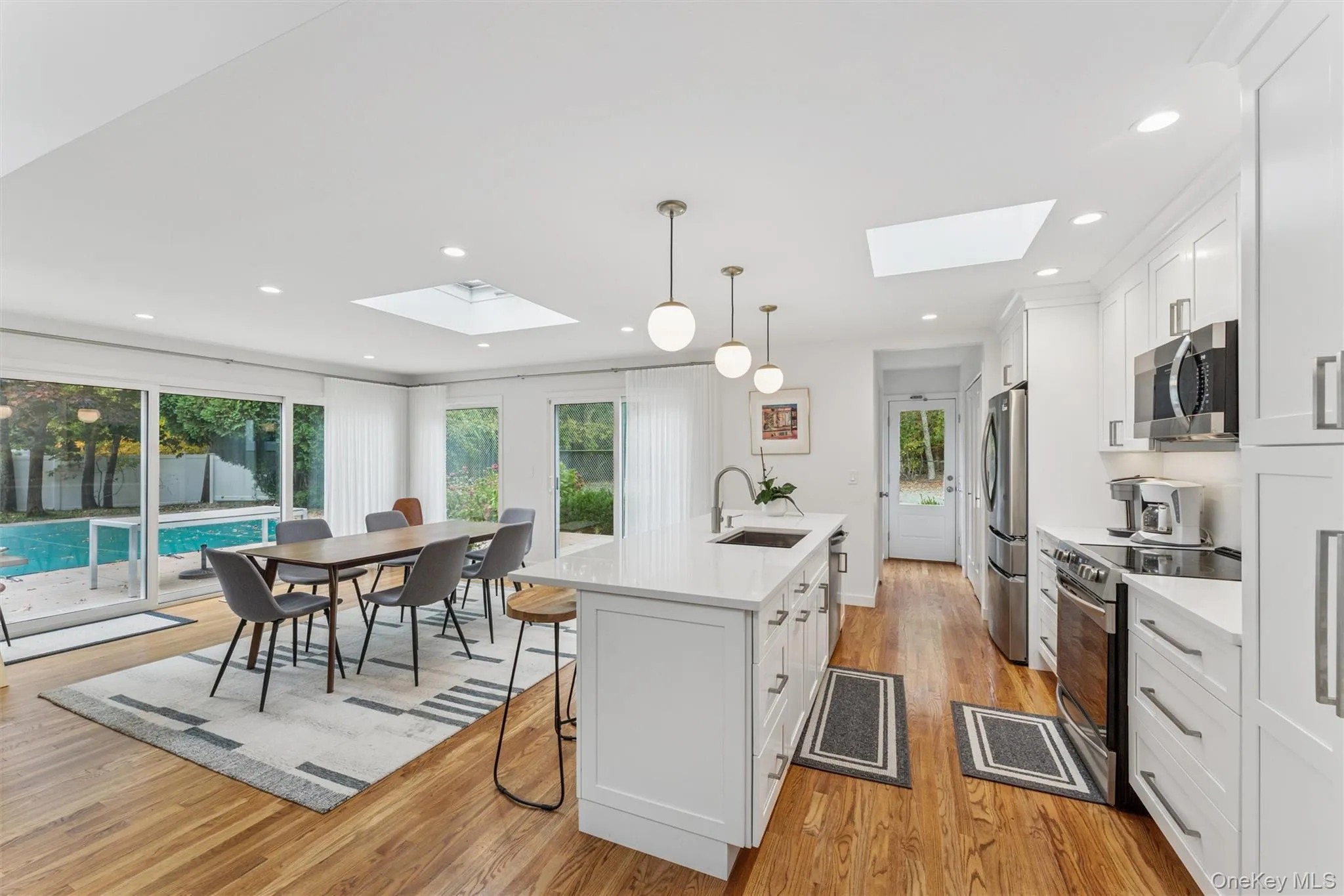 Kitchen with stainless steel appliances, hanging light fixtures, an island with sink, a kitchen bar, and white cabinets Kitchen with stainless steel appliances, hanging light fixtures, an island with sink, a kitchen bar, and white cabinets