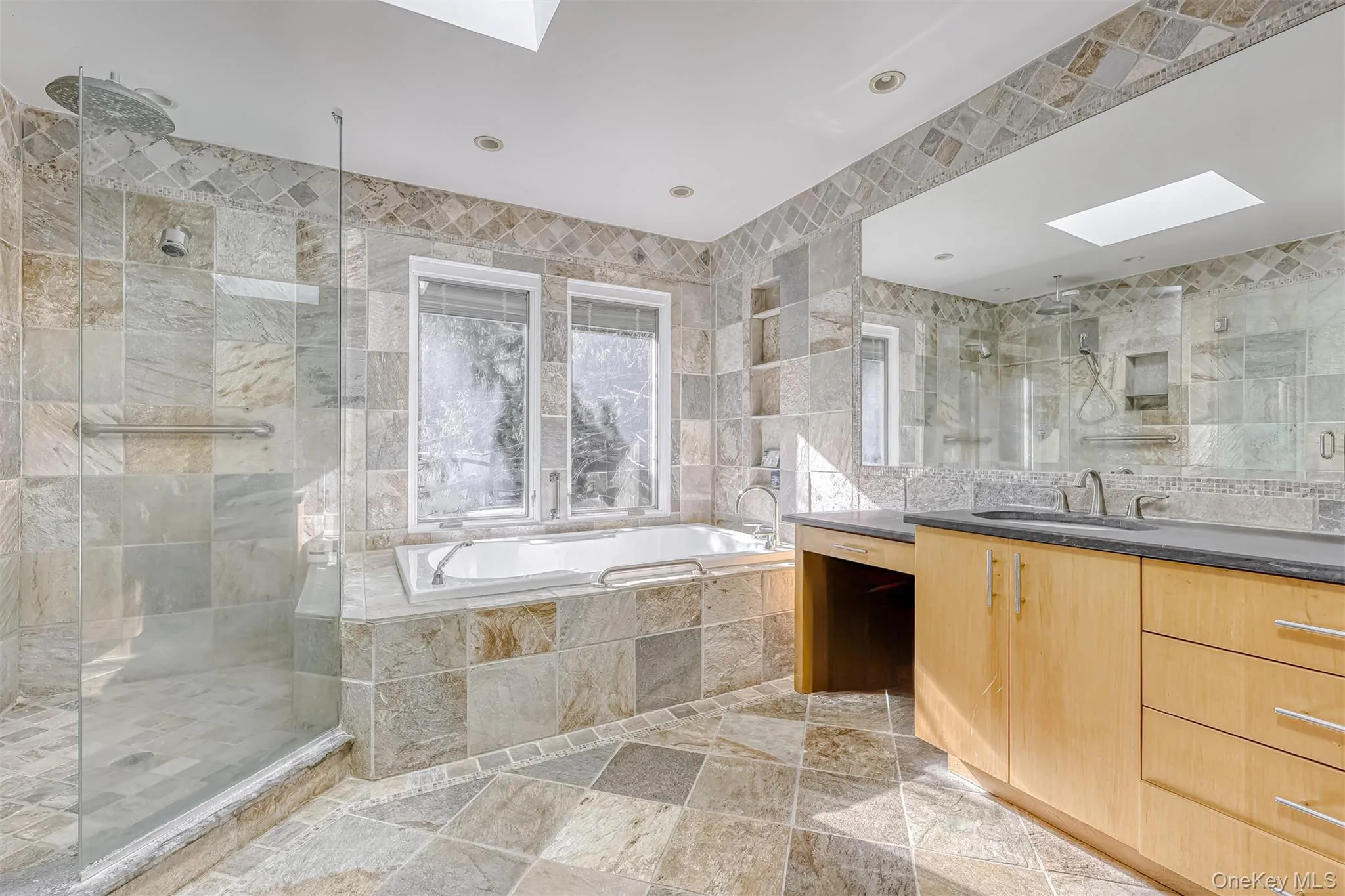 Full bathroom featuring a skylight, tile walls, a bath, vanity, and a stall shower Full bathroom featuring a skylight, tile walls, a bath, vanity, and a stall shower
