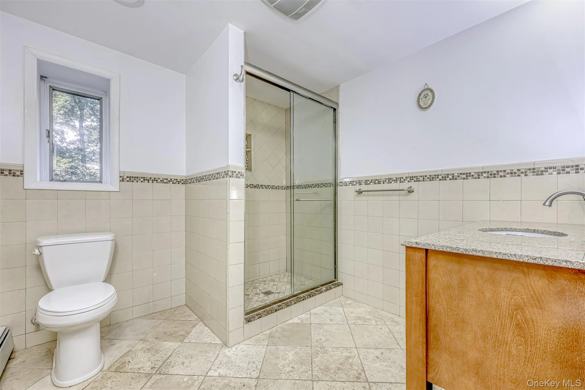 Full bath featuring tile walls, vanity, wainscoting, a stall shower, and light tile patterned flooring Full bath featuring tile walls, vanity, wainscoting, a stall shower, and light tile patterned flooring