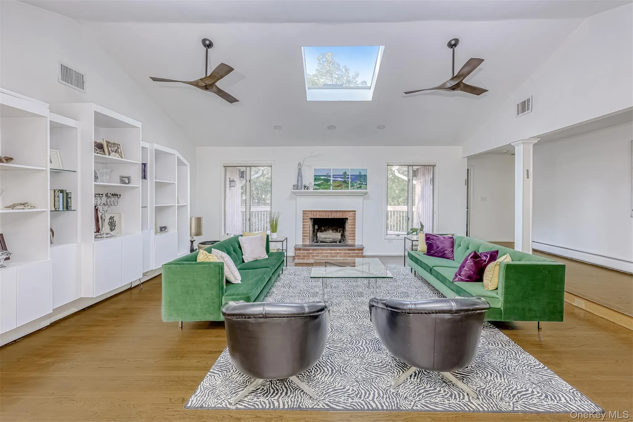 Living area featuring a ceiling fan, high vaulted ceiling, wood finished floors, a fireplace, and a baseboard heating unit Living area featuring a ceiling fan, high vaulted ceiling, wood finished floors, a fireplace, and a baseboard heating unit