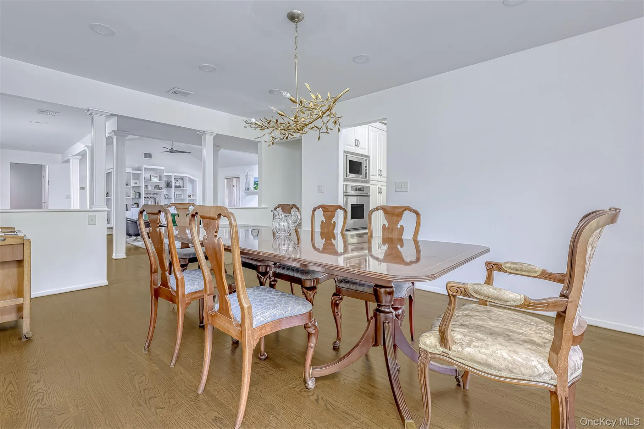 Dining space featuring decorative columns, wood finished floors, a ceiling fan, and a chandelier Dining space featuring decorative columns, wood finished floors, a ceiling fan, and a chandelier