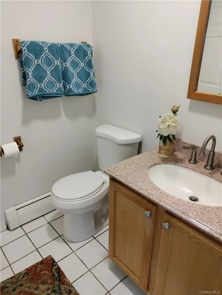 Bathroom with tile floors, toilet, vanity, and a baseboard radiator Bathroom with tile floors, toilet, vanity, and a baseboard radiator