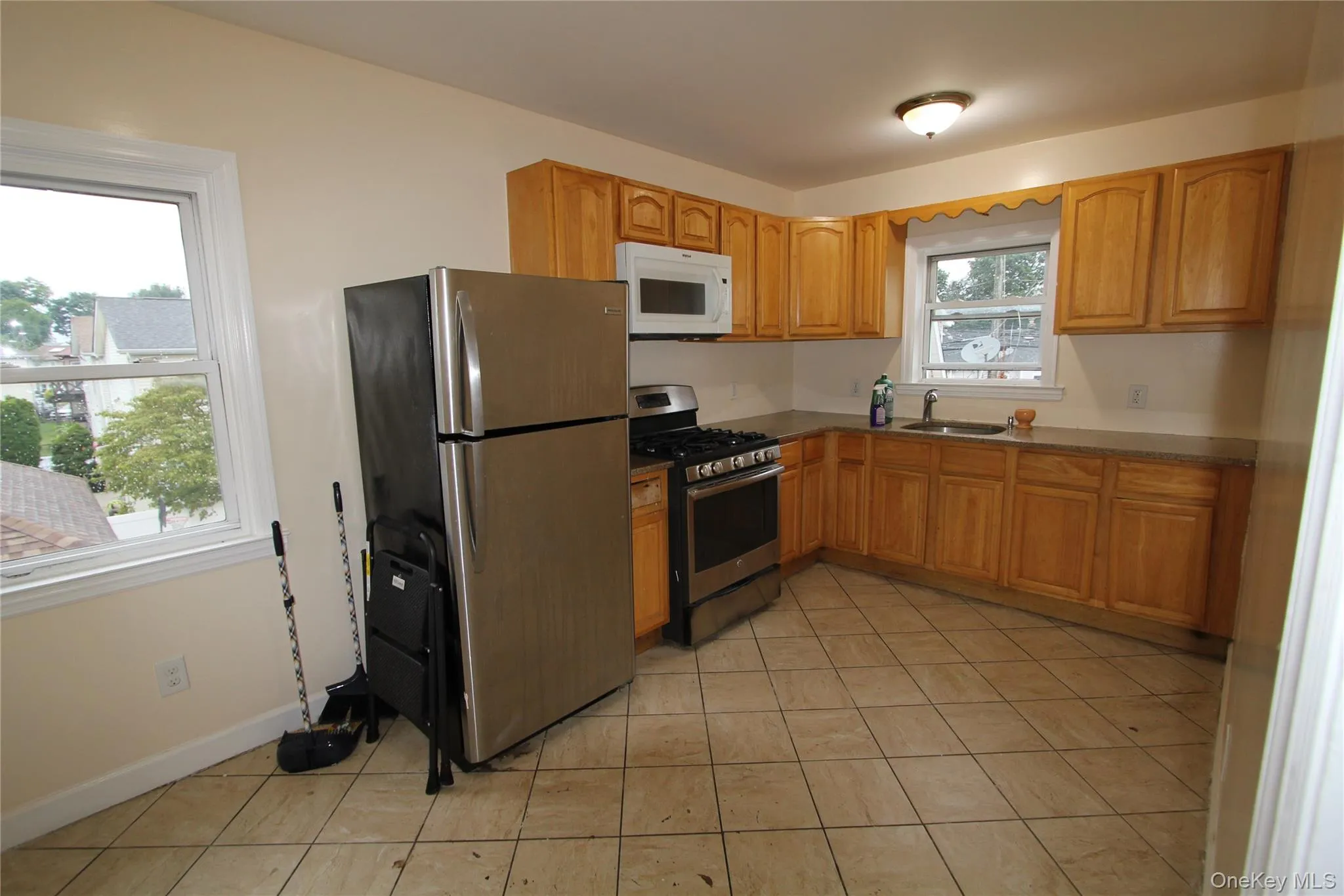 Kitchen featuring appliances with stainless steel finishes, light tile patterned floors, and brown cabinetry Kitchen featuring appliances with stainless steel finishes, light tile patterned floors, and brown cabinetry
