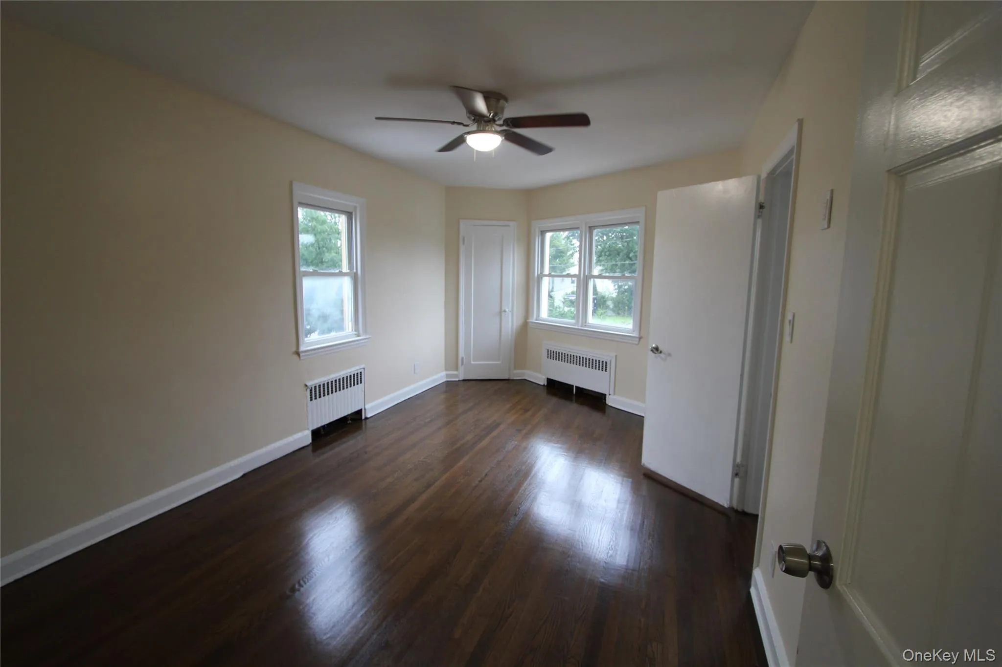 Unfurnished bedroom with dark wood-style flooring, multiple windows, and radiator Unfurnished bedroom with dark wood-style flooring, multiple windows, and radiator