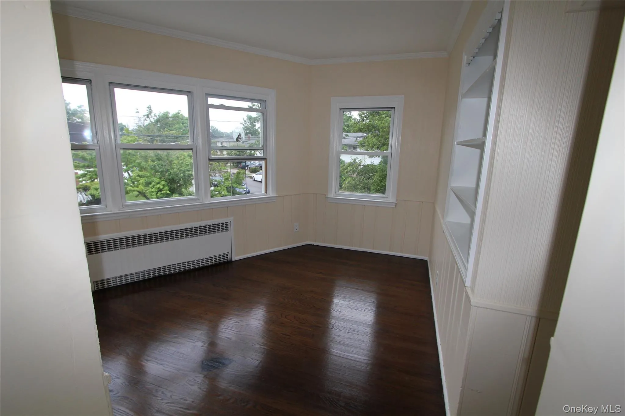 Unfurnished room with crown molding, radiator, and dark wood finished floors Unfurnished room with crown molding, radiator, and dark wood finished floors