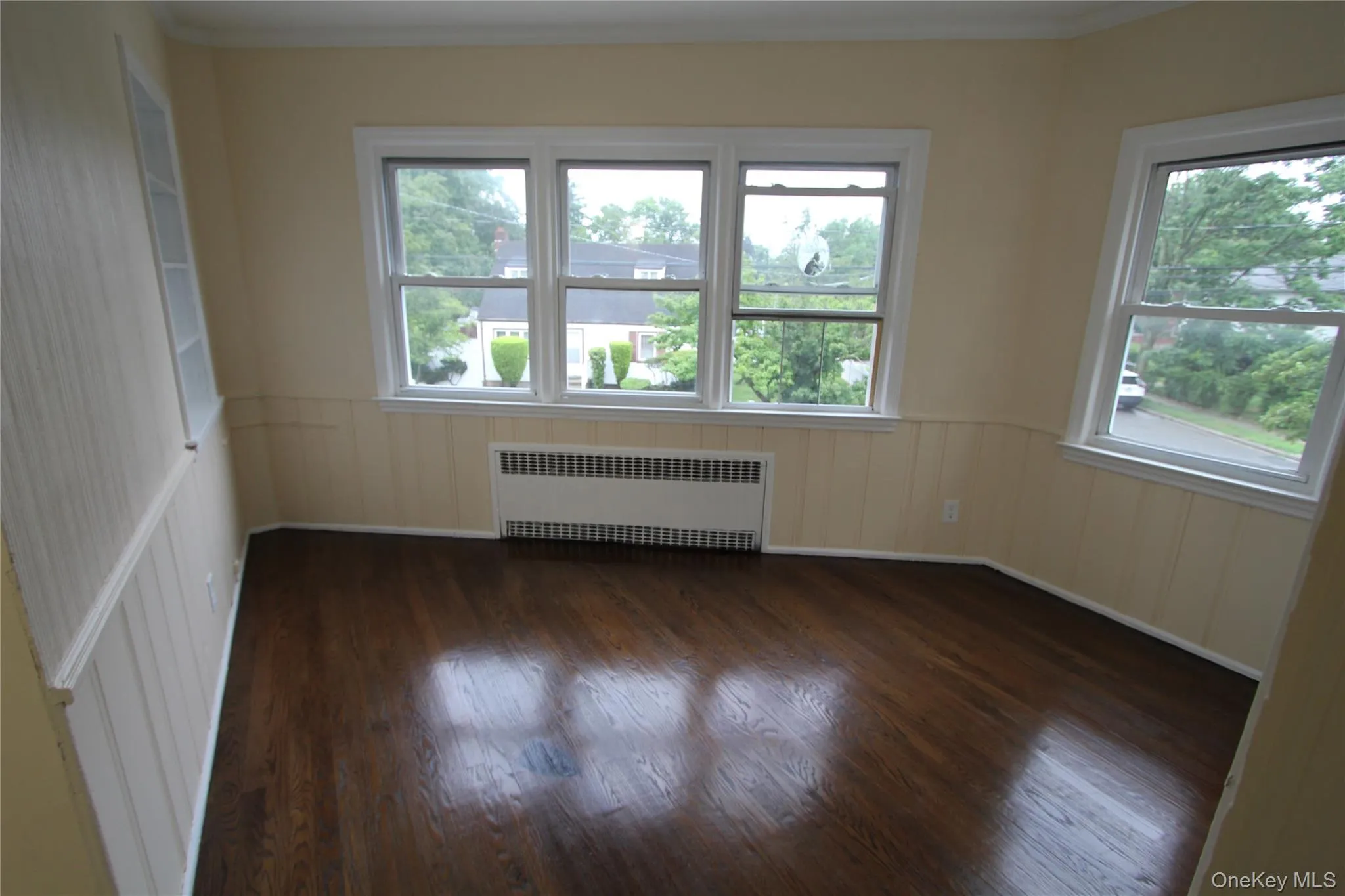 Spare room featuring plenty of natural light, radiator, dark wood-style flooring, crown molding, and a wainscoted wall Spare room featuring plenty of natural light, radiator, dark wood-style flooring, crown molding, and a wainscoted wall