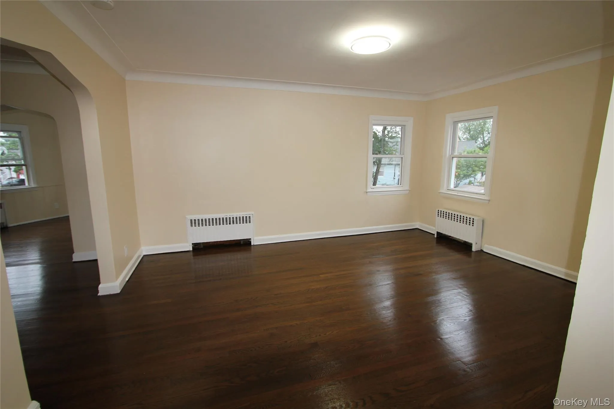 Spare room featuring arched walkways, radiator, dark wood-style flooring, and ornamental molding Spare room featuring arched walkways, radiator, dark wood-style flooring, and ornamental molding