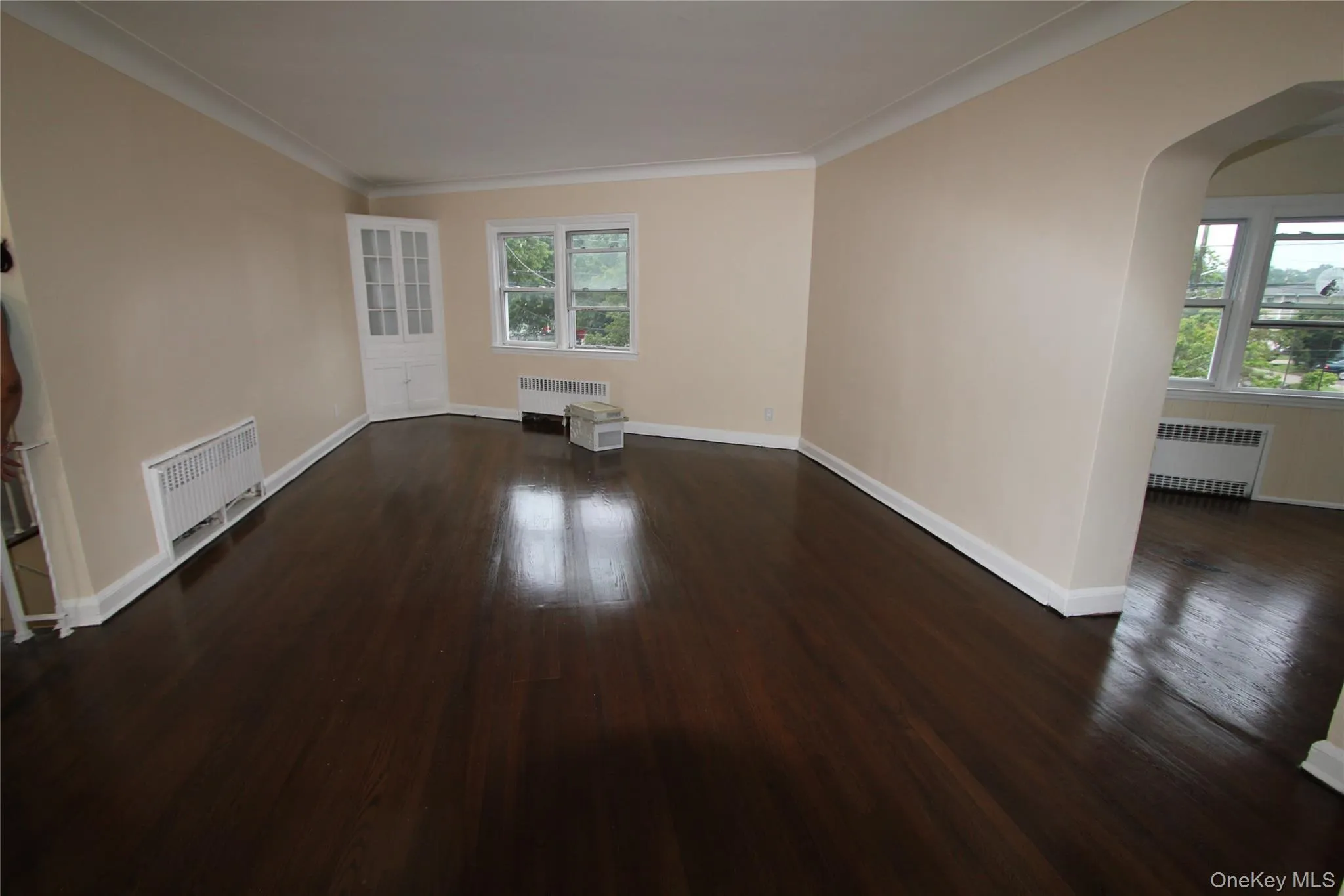 Empty room featuring dark wood-style floors, arched walkways, ornamental molding, and radiator Empty room featuring dark wood-style floors, arched walkways, ornamental molding, and radiator