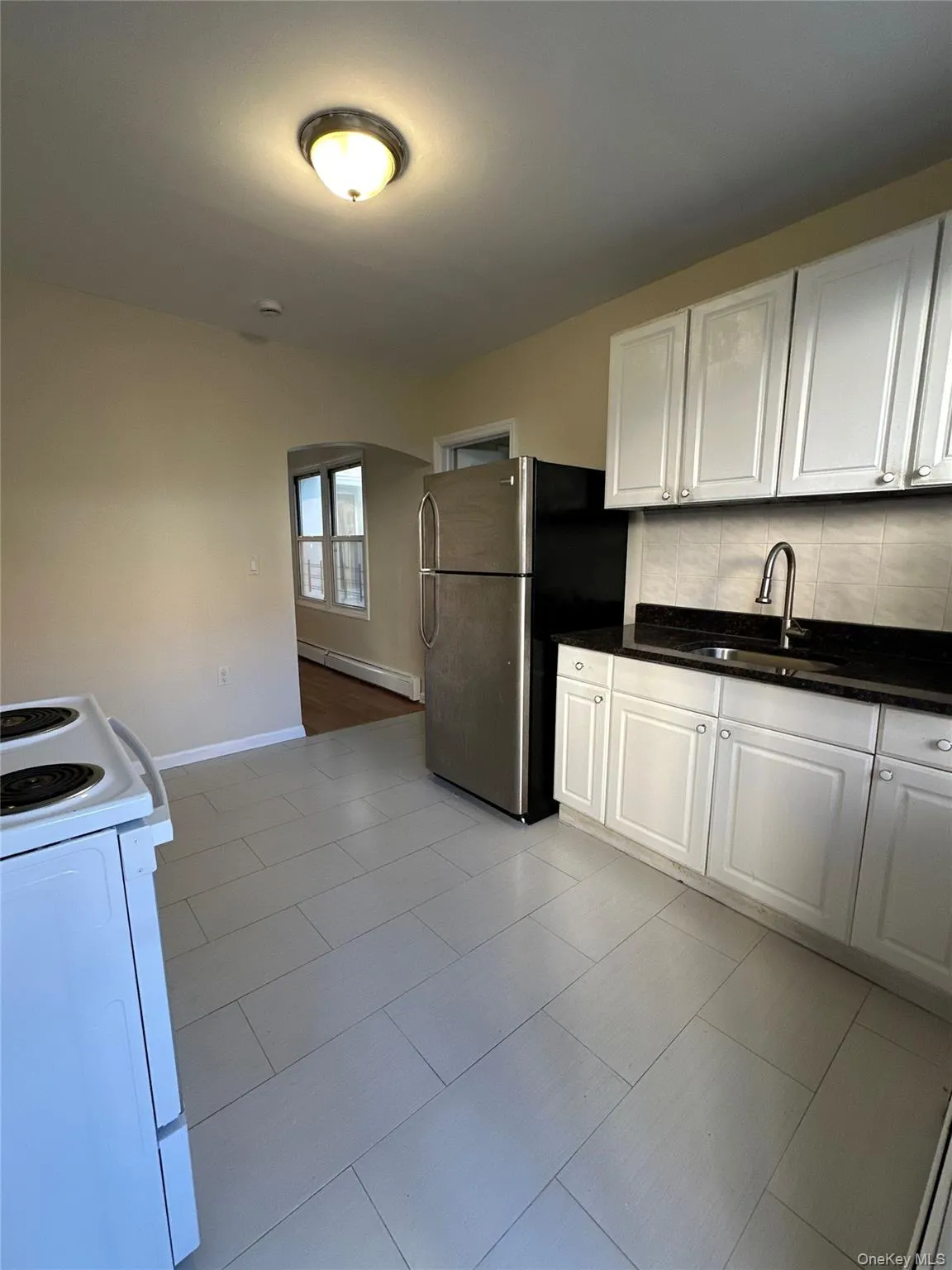 Kitchen with electric range, white cabinets, freestanding refrigerator, a baseboard radiator, and backsplash Kitchen with electric range, white cabinets, freestanding refrigerator, a baseboard radiator, and backsplash