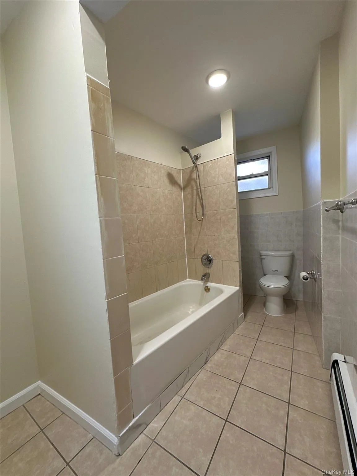 Bathroom featuring light tile patterned flooring, baseboard heating, shower combination, and tile walls Bathroom featuring light tile patterned flooring, baseboard heating, shower combination, and tile walls