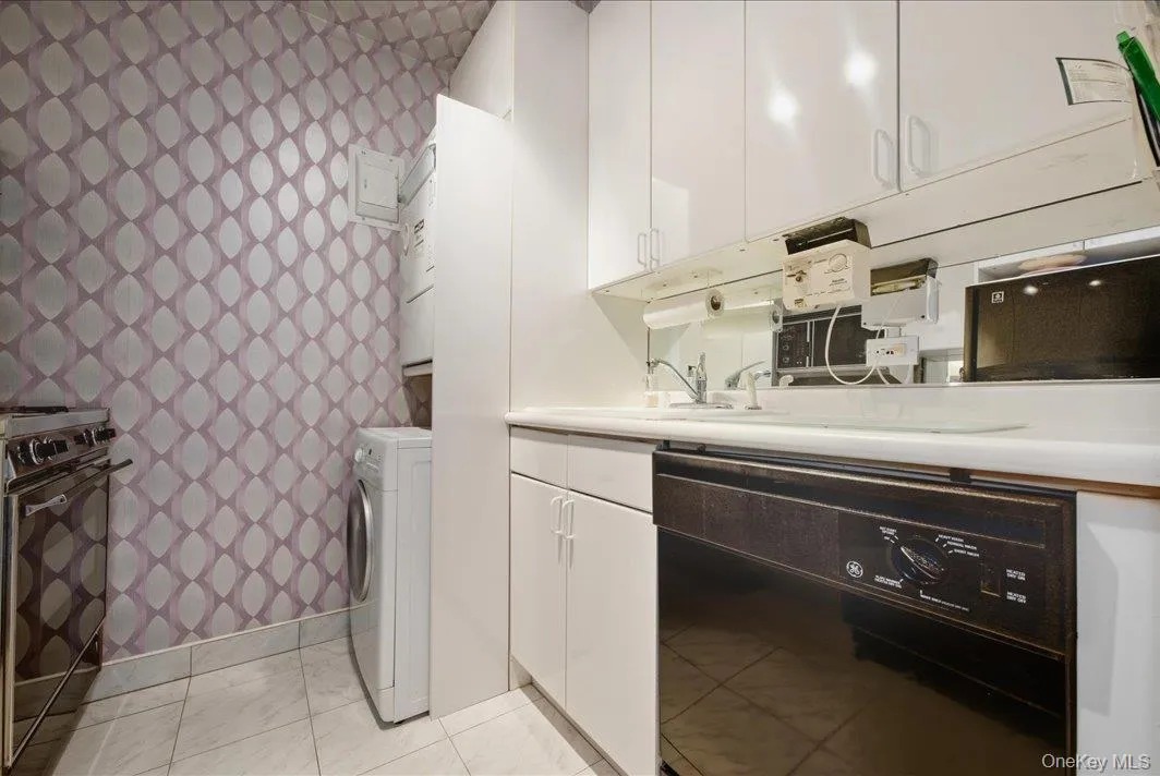 Laundry area featuring washer / dryer, wallpapered walls, and light tile patterned flooring Laundry area featuring washer / dryer, wallpapered walls, and light tile patterned flooring