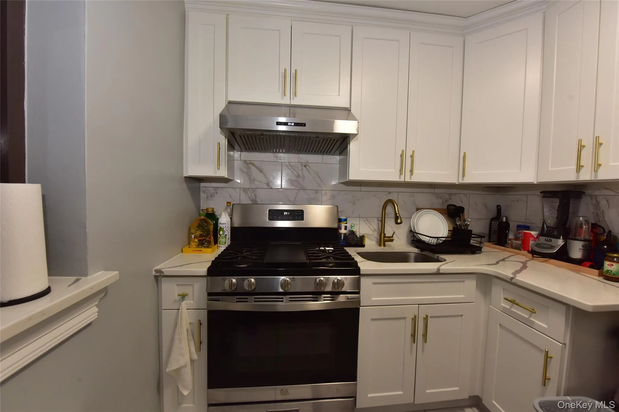 Kitchen with stainless steel gas range oven, white cabinets, under cabinet range hood, tasteful backsplash, and light stone countertops Kitchen with stainless steel gas range oven, white cabinets, under cabinet range hood, tasteful backsplash, and light stone countertops