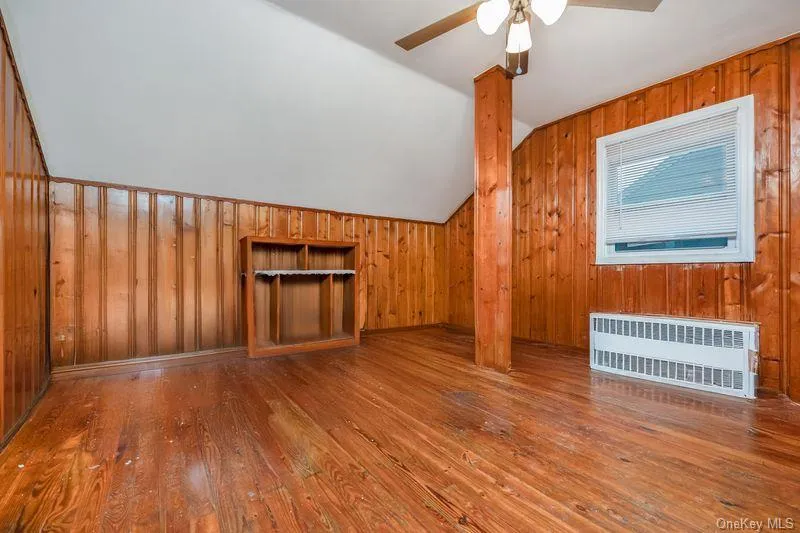 Bonus room featuring wooden walls, lofted ceiling, radiator heating unit, and hardwood / wood-style flooring Bonus room featuring wooden walls, lofted ceiling, radiator heating unit, and hardwood / wood-style flooring