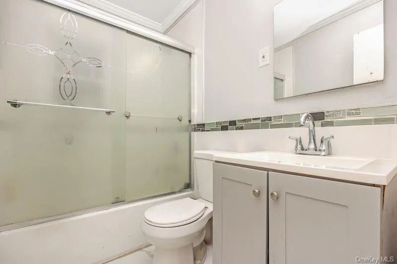 Bathroom featuring vanity, shower / bath combination with glass door, crown molding, and decorative backsplash Bathroom featuring vanity, shower / bath combination with glass door, crown molding, and decorative backsplash