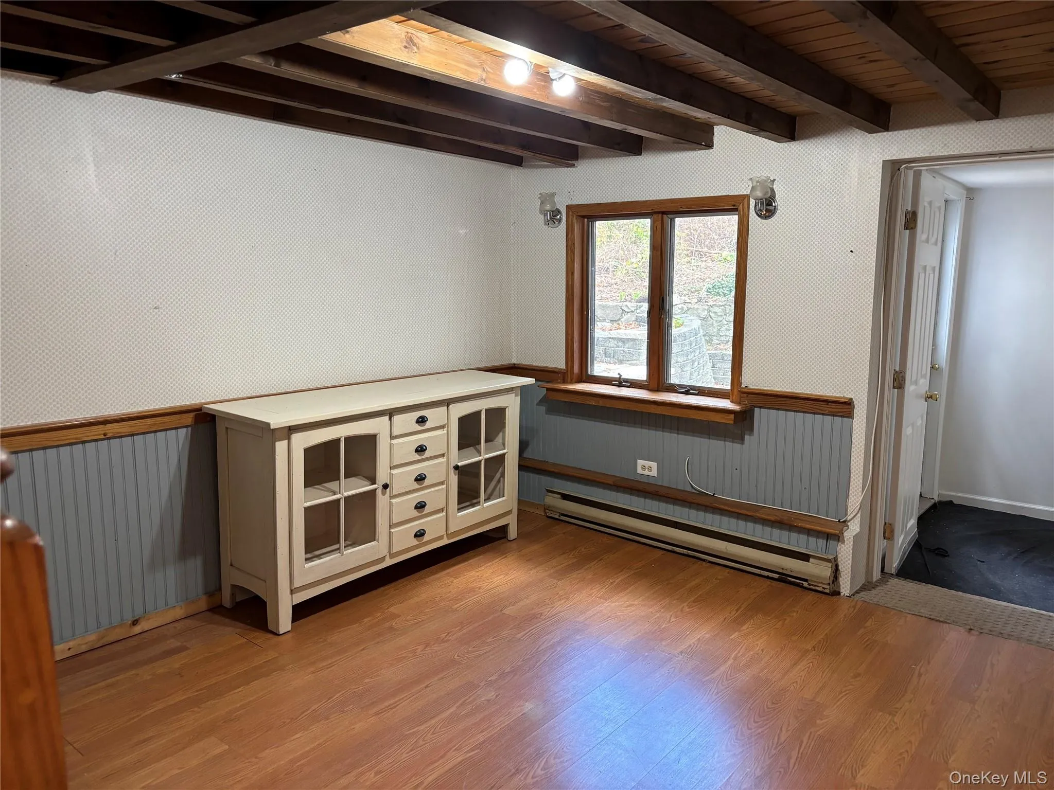 Spare room with baseboard heating, light wood-style flooring, a wood ceiling with exposed beams, and wainscoting Spare room with baseboard heating, light wood-style flooring, a wood ceiling with exposed beams, and wainscoting