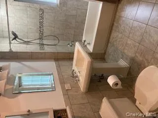 Full bath with shower / tub combo, tile walls, wainscoting, and light tile patterned floors Full bath with shower / tub combo, tile walls, wainscoting, and light tile patterned floors