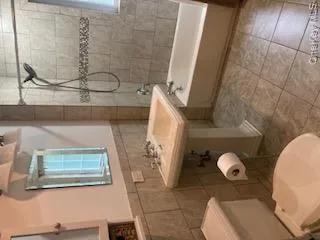 Full bath with shower / tub combo, tile walls, wainscoting, and light tile patterned floors Full bath with shower / tub combo, tile walls, wainscoting, and light tile patterned floors