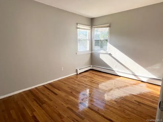 Unfurnished room with light wood-type flooring and a baseboard radiator Unfurnished room with light wood-type flooring and a baseboard radiator