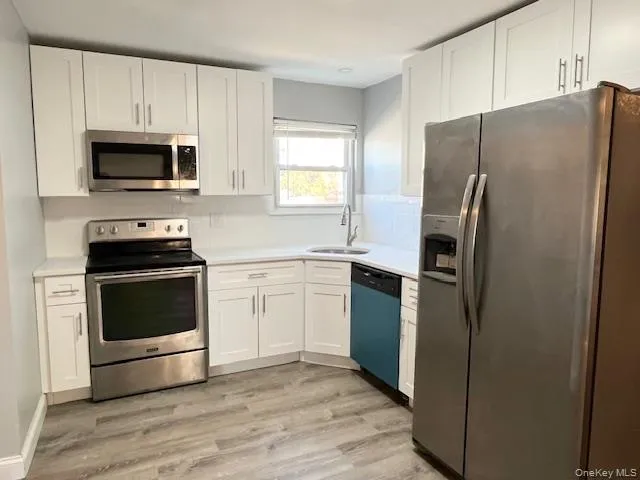 Kitchen featuring stainless steel appliances, white cabinetry, light countertops, backsplash, and light wood finished floors Kitchen featuring stainless steel appliances, white cabinetry, light countertops, backsplash, and light wood finished floors