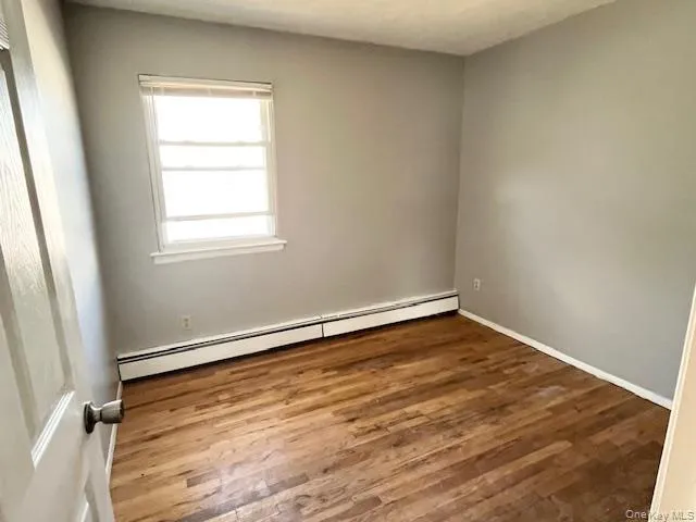 Unfurnished room featuring a baseboard radiator and wood finished floors Unfurnished room featuring a baseboard radiator and wood finished floors