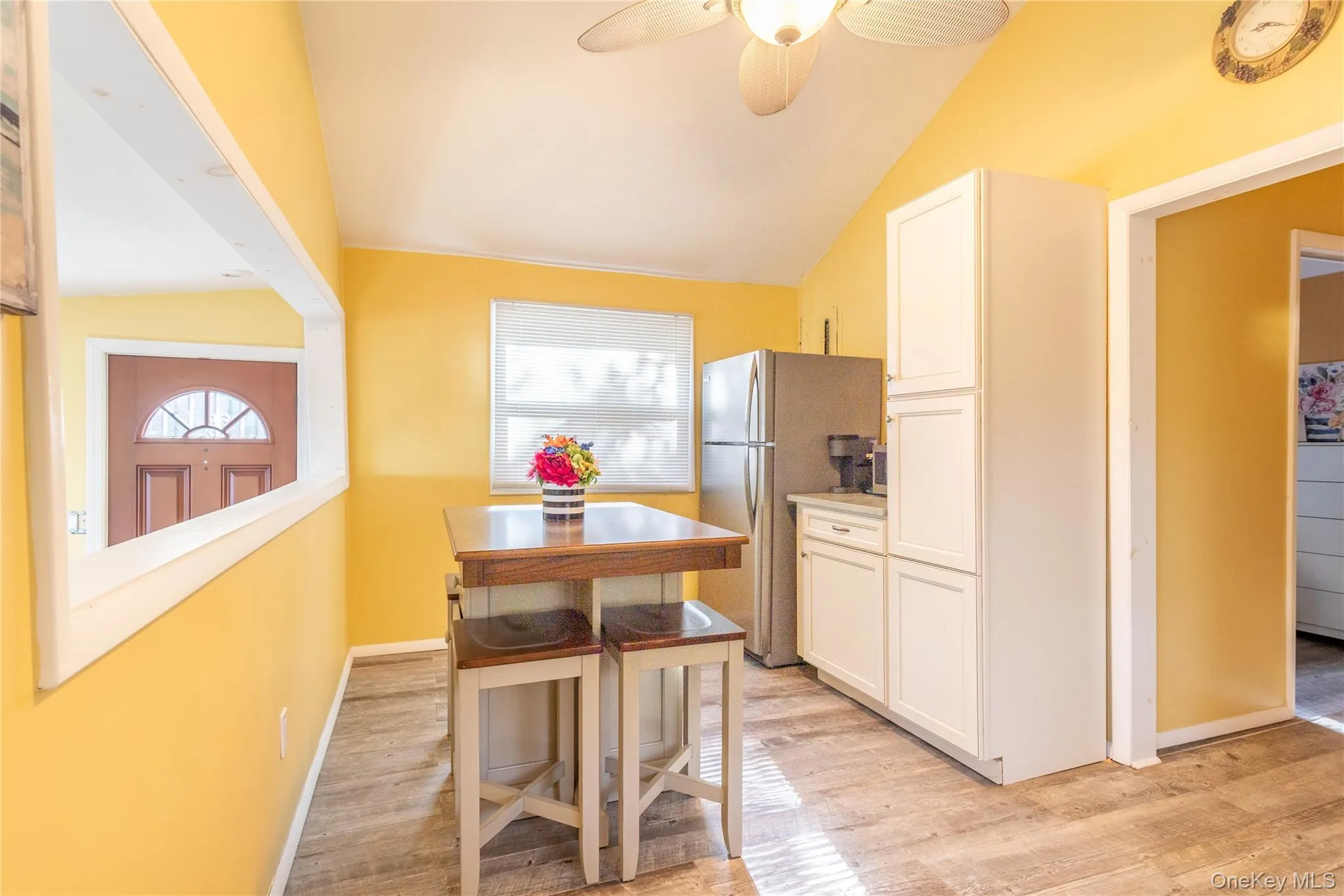 Kitchen with white cabinetry, freestanding refrigerator, light wood-type flooring, light countertops, and vaulted ceiling Kitchen with white cabinetry, freestanding refrigerator, light wood-type flooring, light countertops, and vaulted ceiling