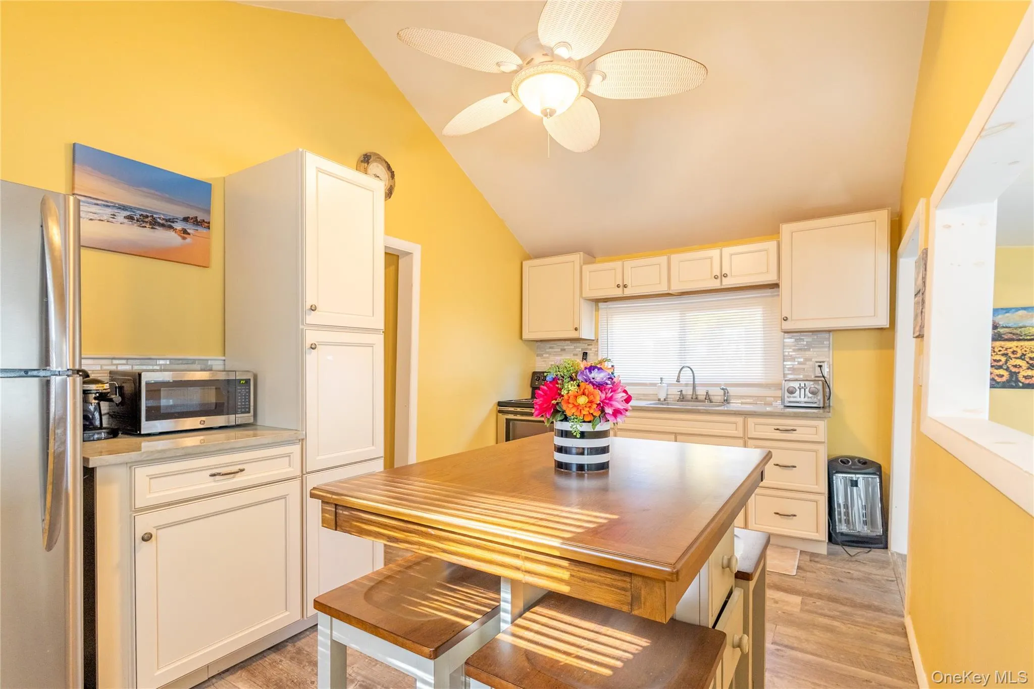 Kitchen featuring stainless steel appliances, decorative backsplash, light wood finished floors, vaulted ceiling, and ceiling fan Kitchen featuring stainless steel appliances, decorative backsplash, light wood finished floors, vaulted ceiling, and ceiling fan