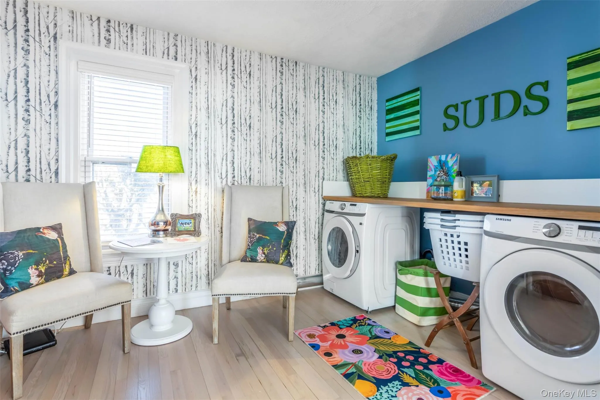 Laundry room featuring wood-type flooring, washing machine and clothes dryer, and wallpapered walls Laundry room featuring wood-type flooring, washing machine and clothes dryer, and wallpapered walls