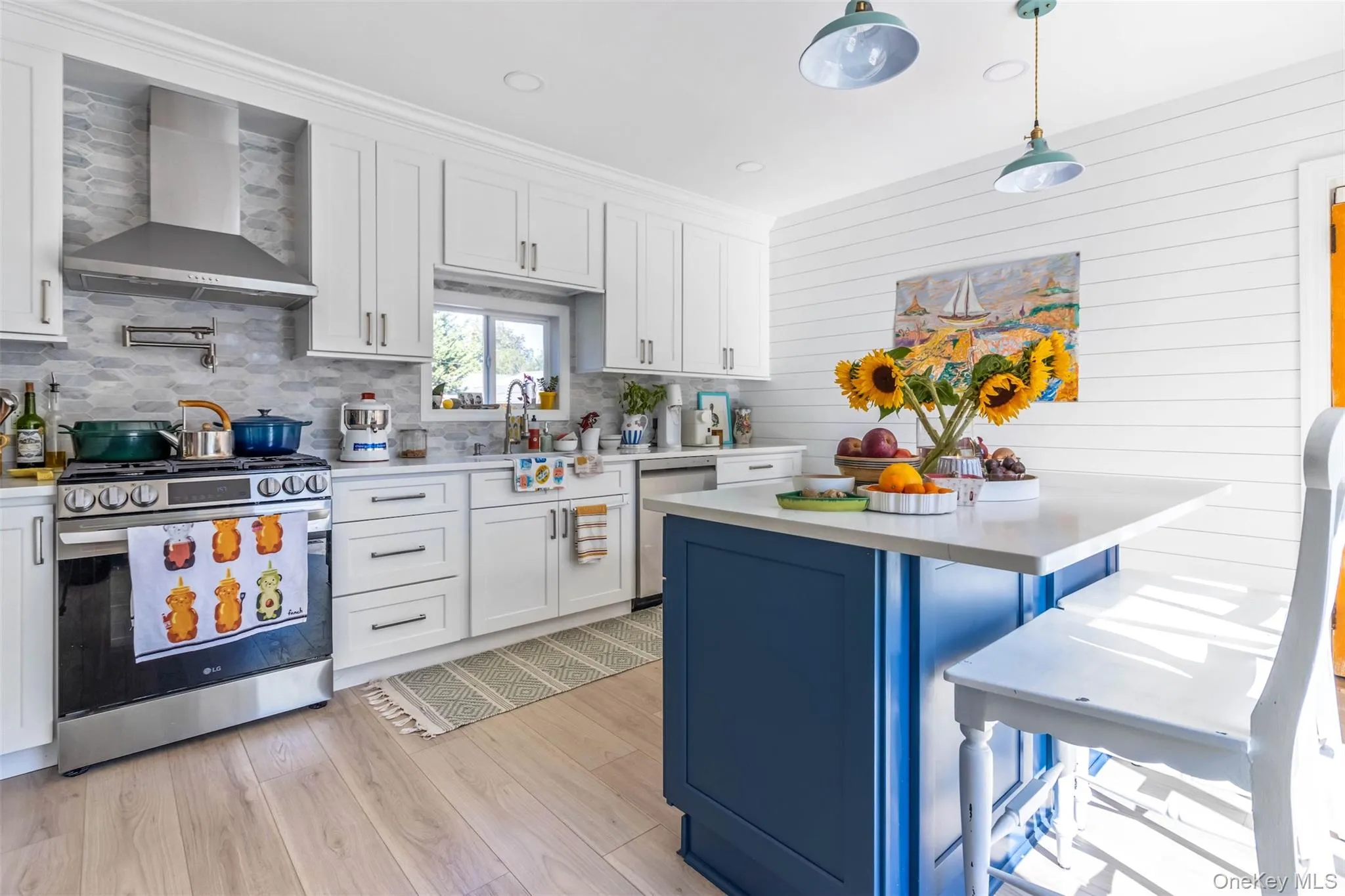 Kitchen featuring blue cabinetry, white cabinets, appliances with stainless steel finishes, wall chimney exhaust hood, and decorative light fixtures Kitchen featuring blue cabinetry, white cabinets, appliances with stainless steel finishes, wall chimney exhaust hood, and decorative light fixtures